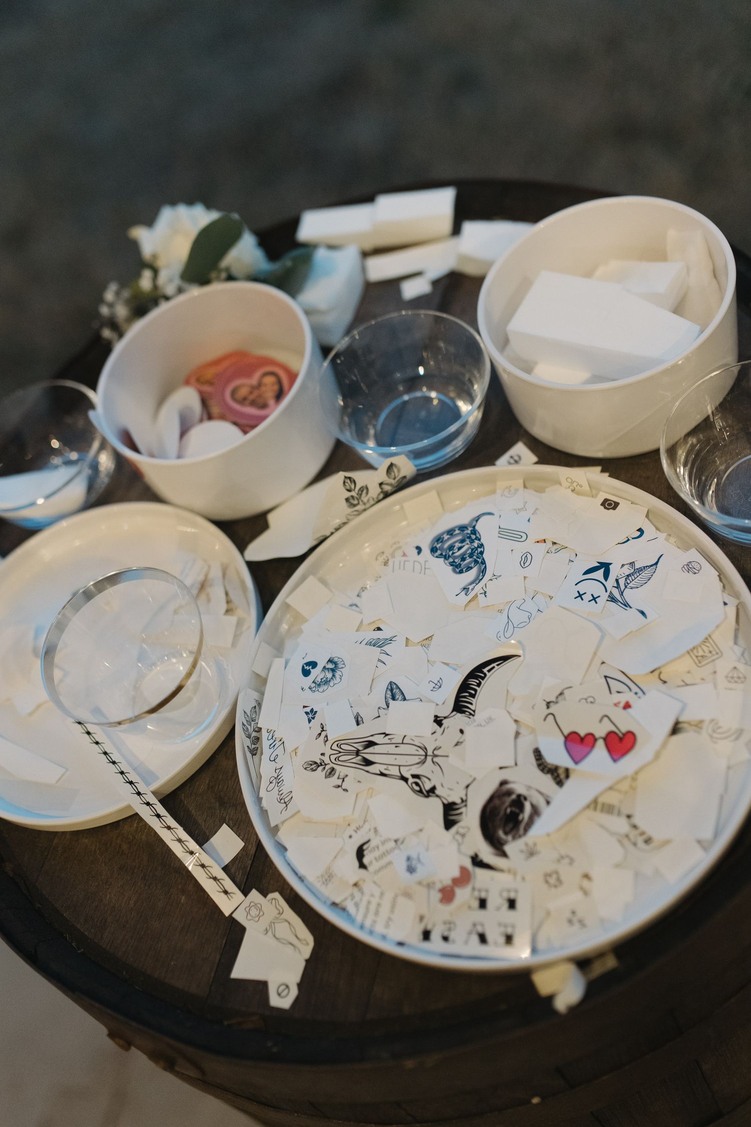 Wedding table display with decorated plate, bowls of candy, glassware, and white cards on a rustic barrel.