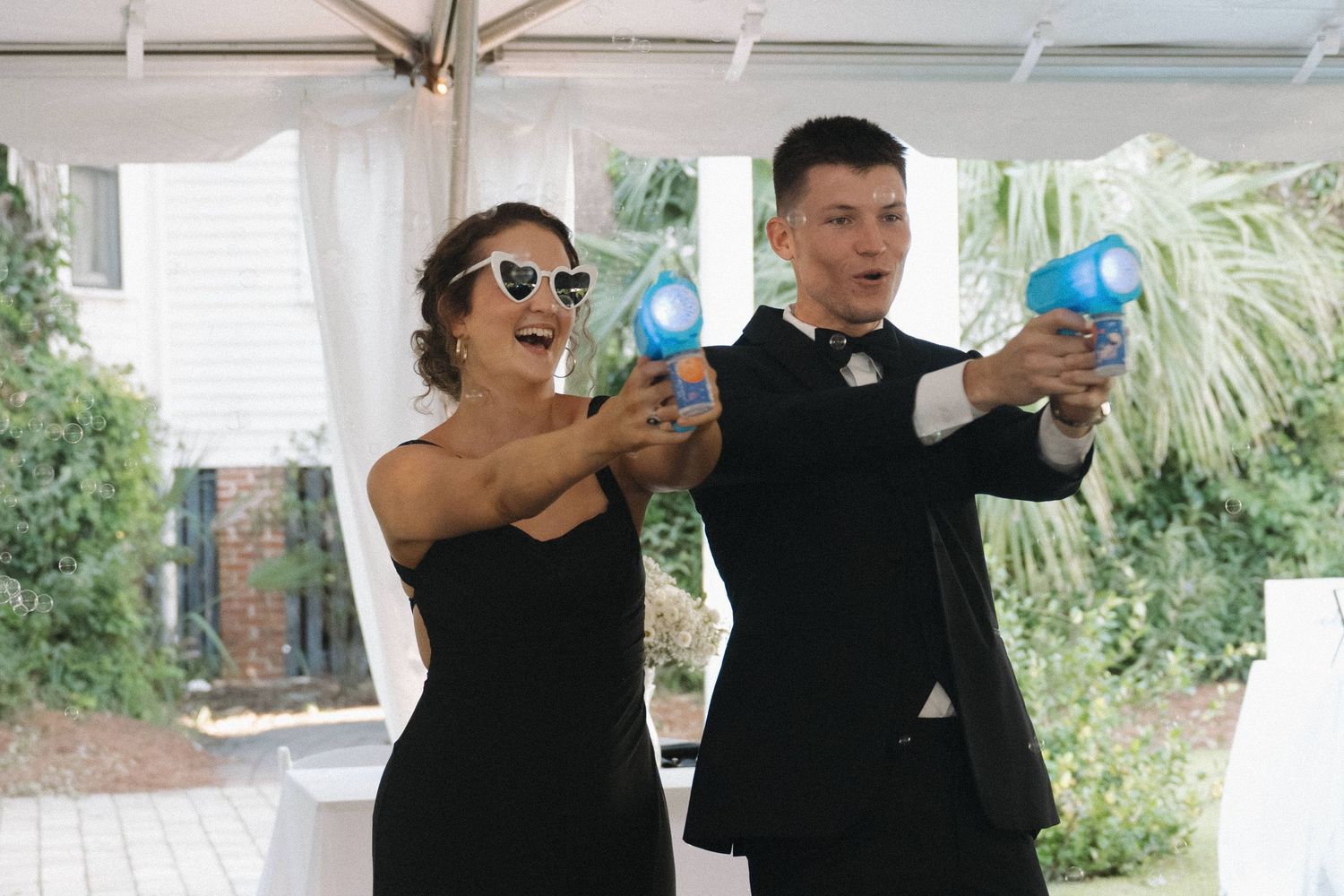 Bridesmaid and groomsman playfully pose with blue water guns at wedding reception.