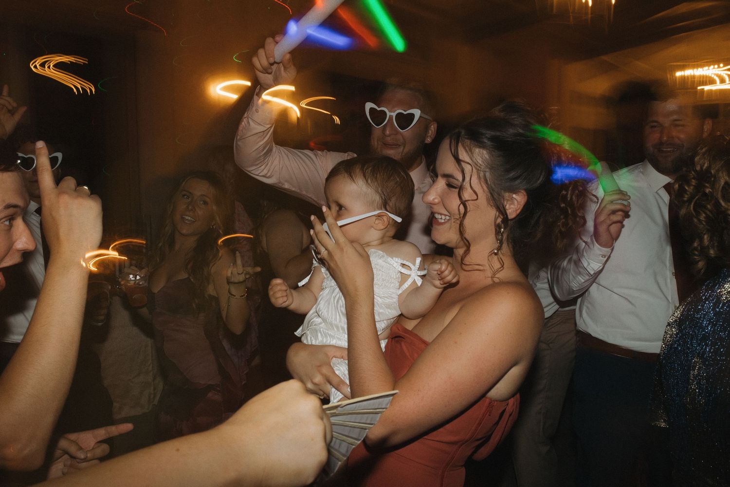 Guests dancing and celebrating at a lively wedding reception party with colorful lights and sparklers.