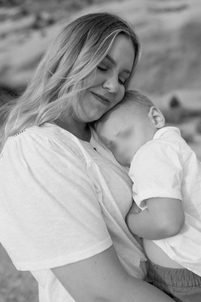 Black and white photo of a smiling mother tenderly embracing her young son outdoors.