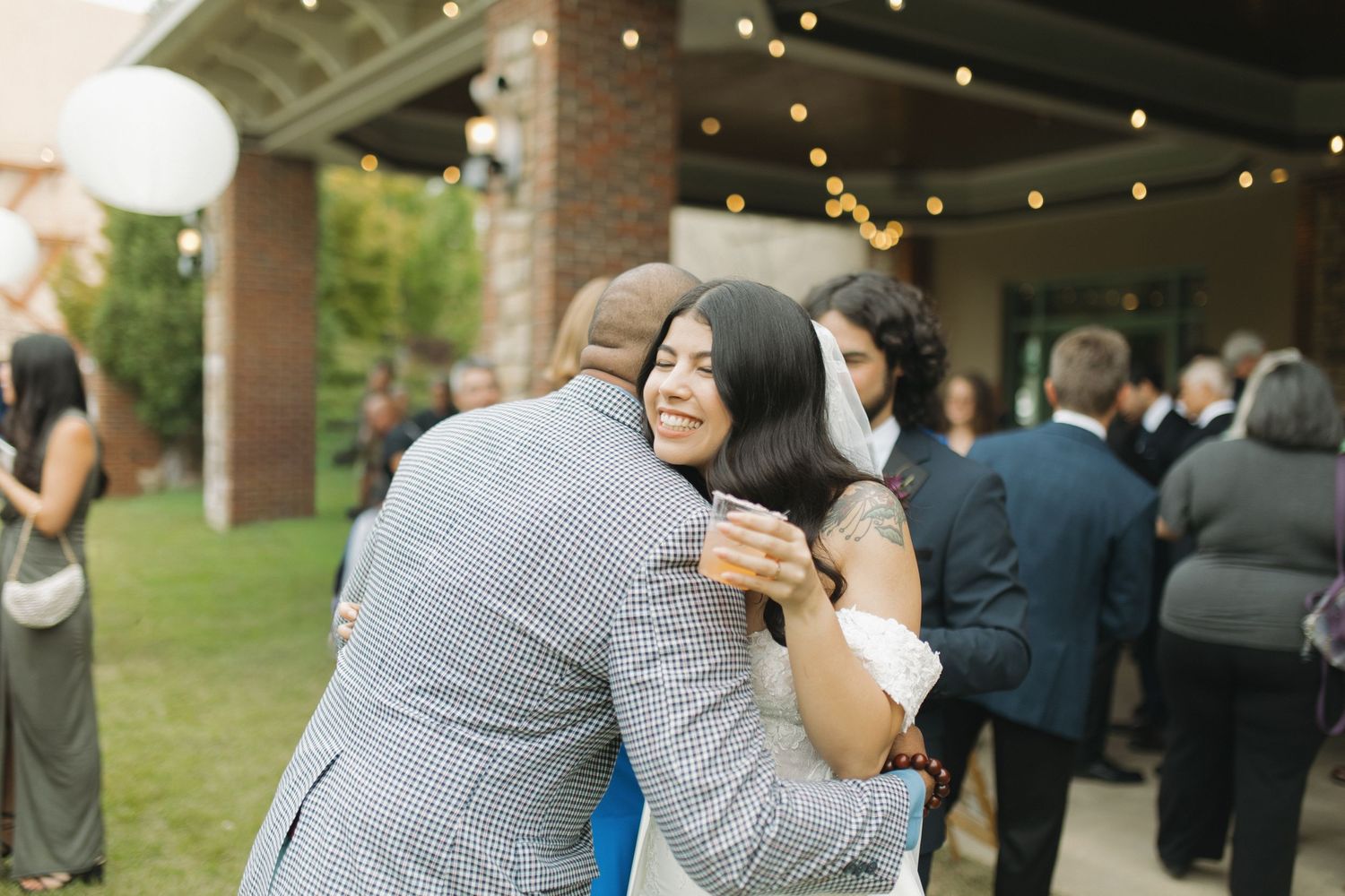 Joyful bride in blue dress hugging wedding guest at outdoor reception.