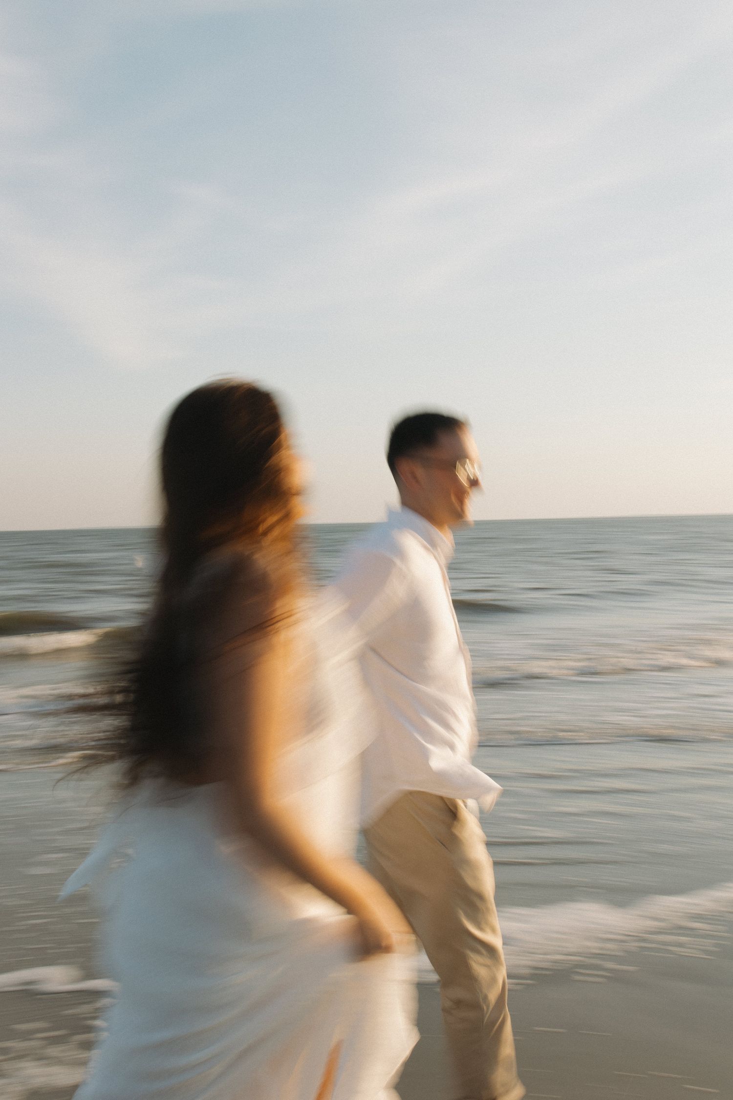 Blurred motion shot of a couple in white walking along the ocean shore at sunset.