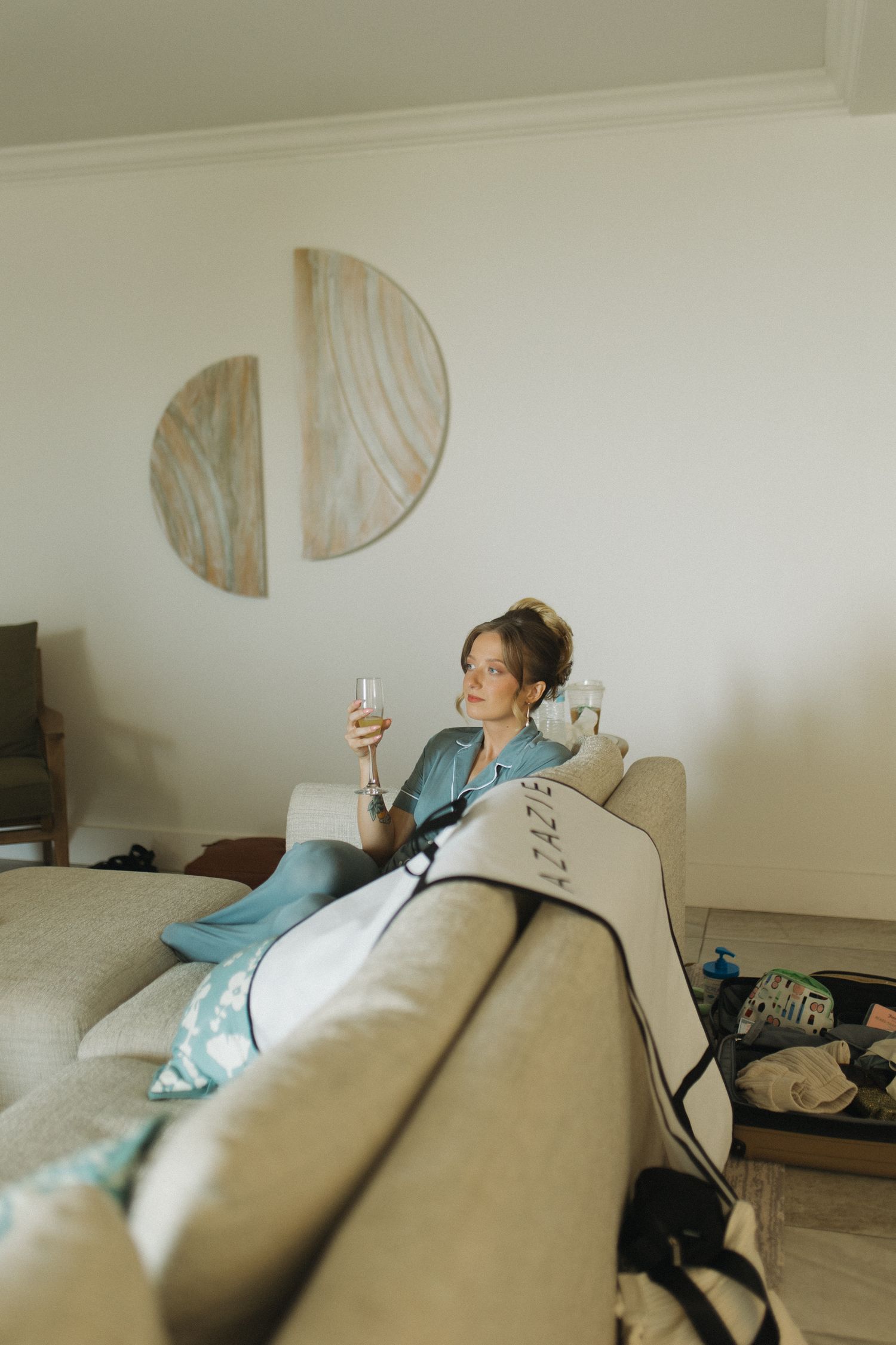 Woman relaxing on sofa using compression leg therapy device while holding a glass in a modern living room.
