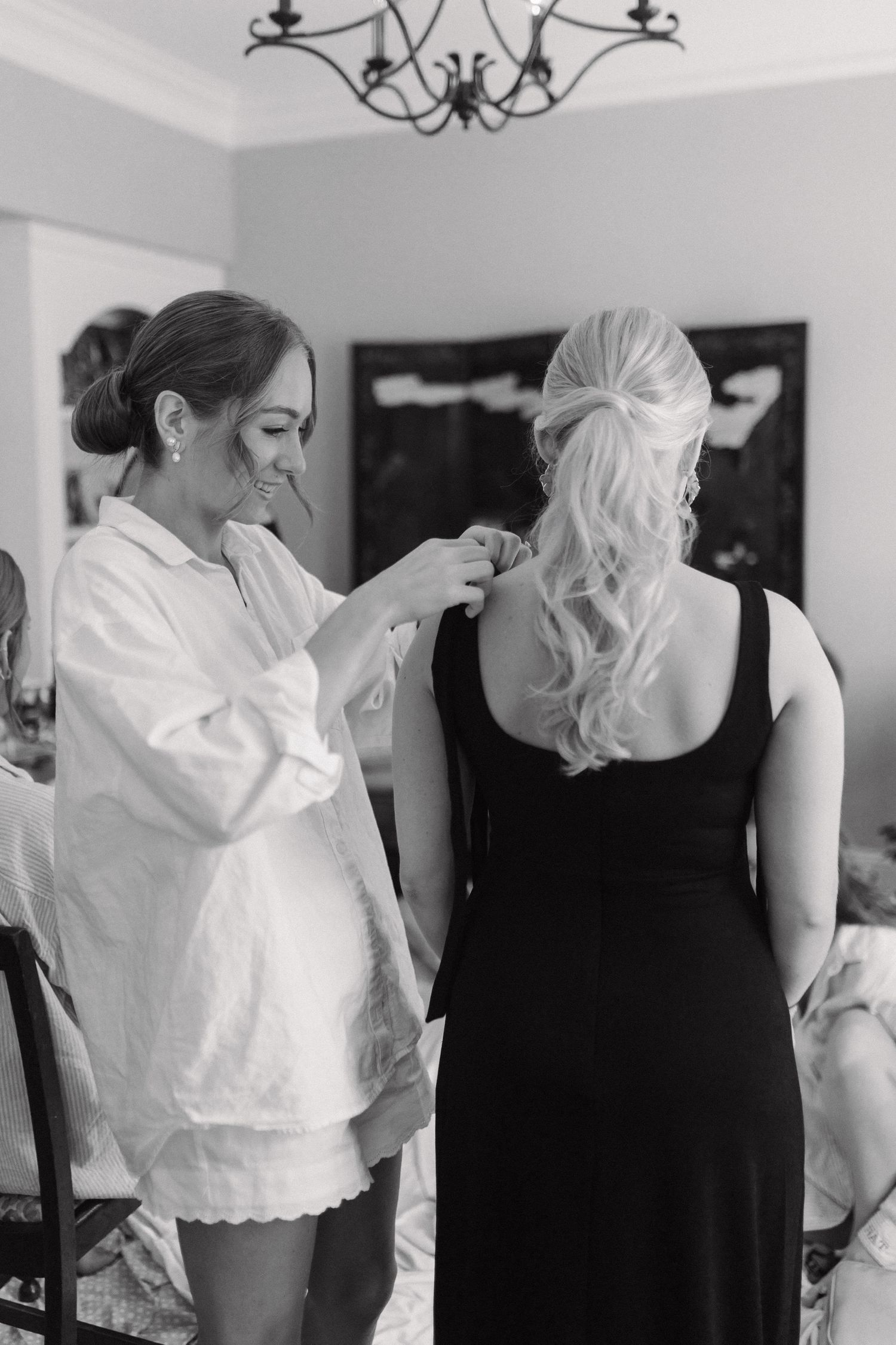 Black and white photo of a woman helping a bridesmaid with her hair before a wedding.