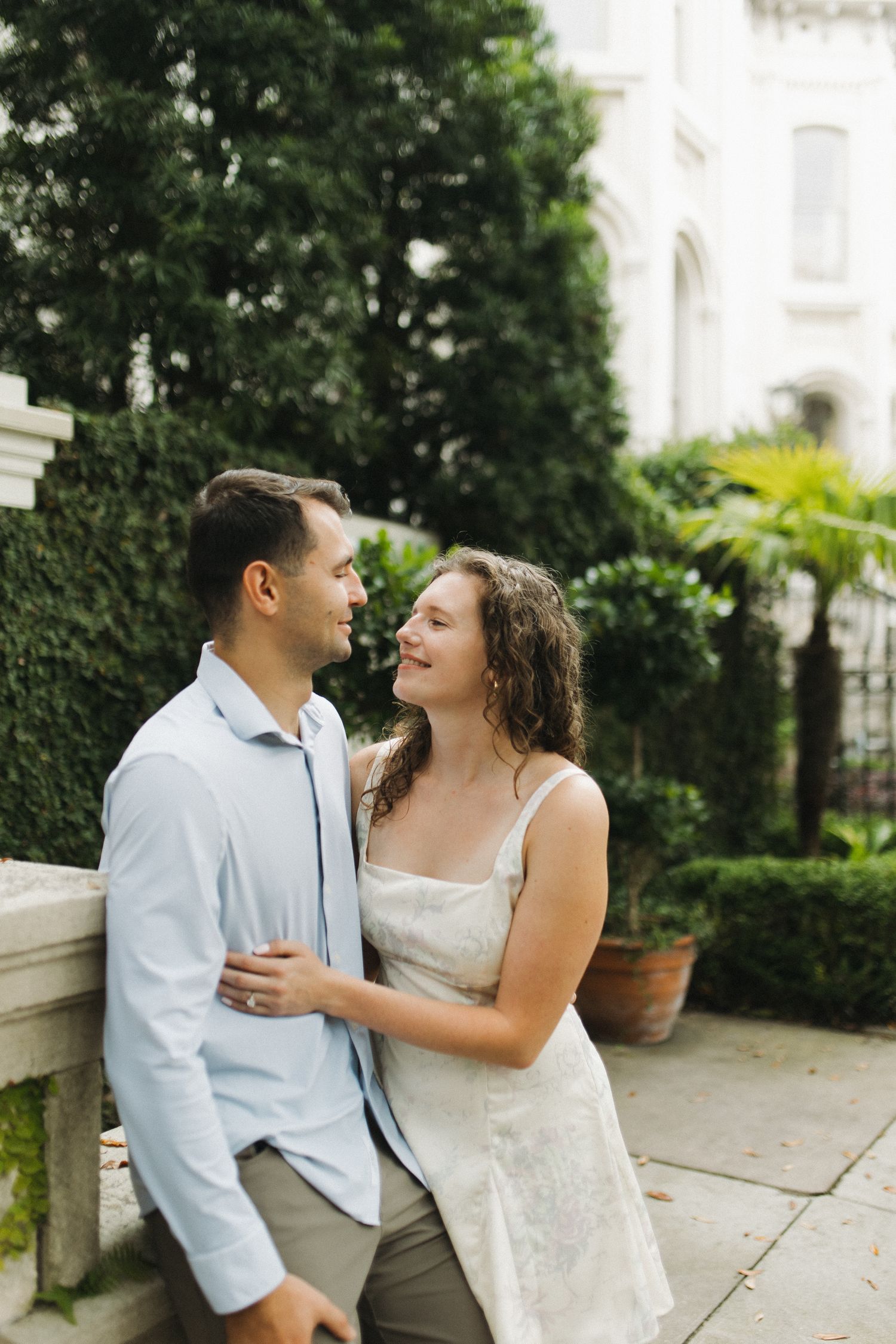 Happy couple smiling at each other outdoors surrounded by lush green foliage.