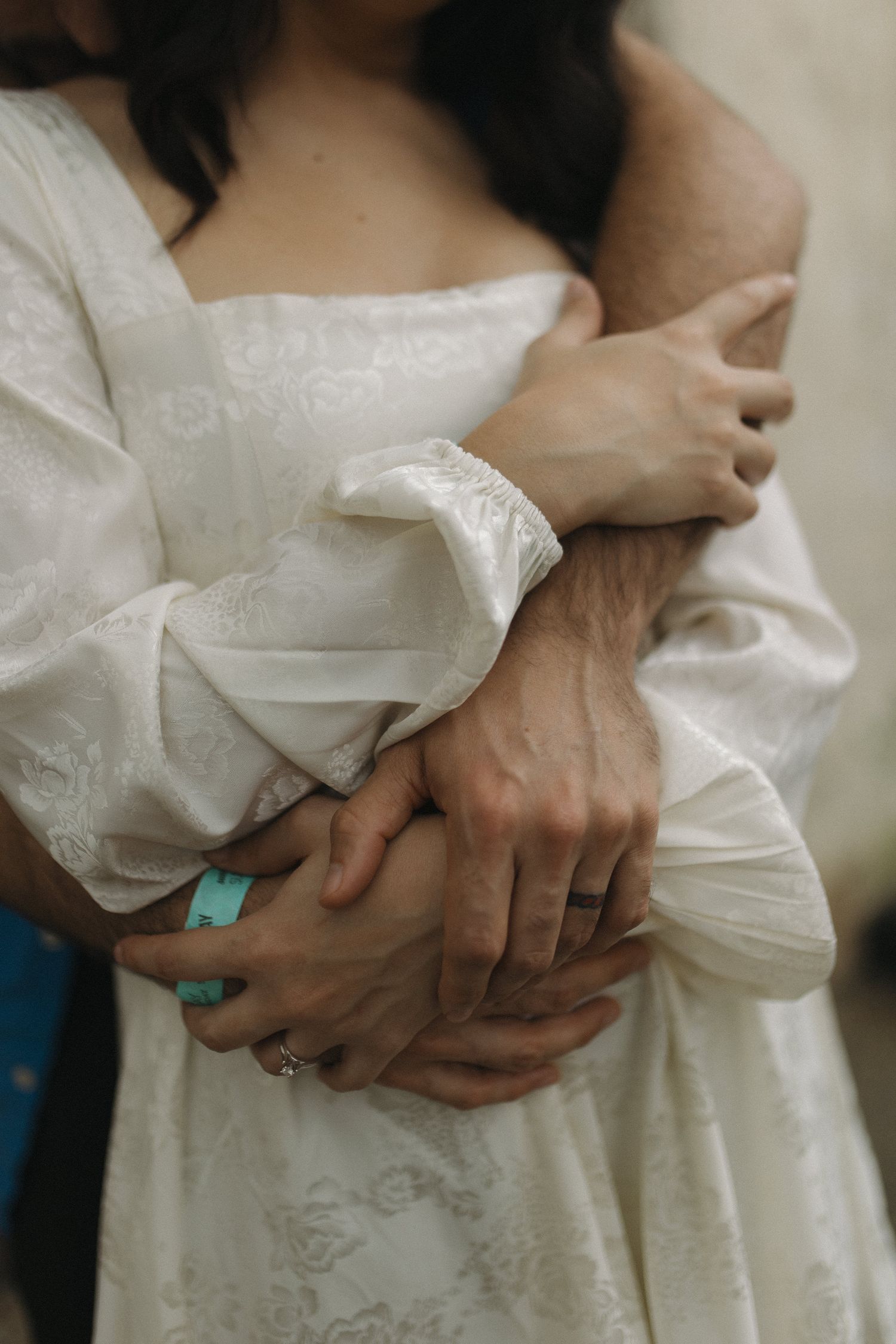 Close-up of a couple holding hands, showcasing an engagement ring and teal bracelet.