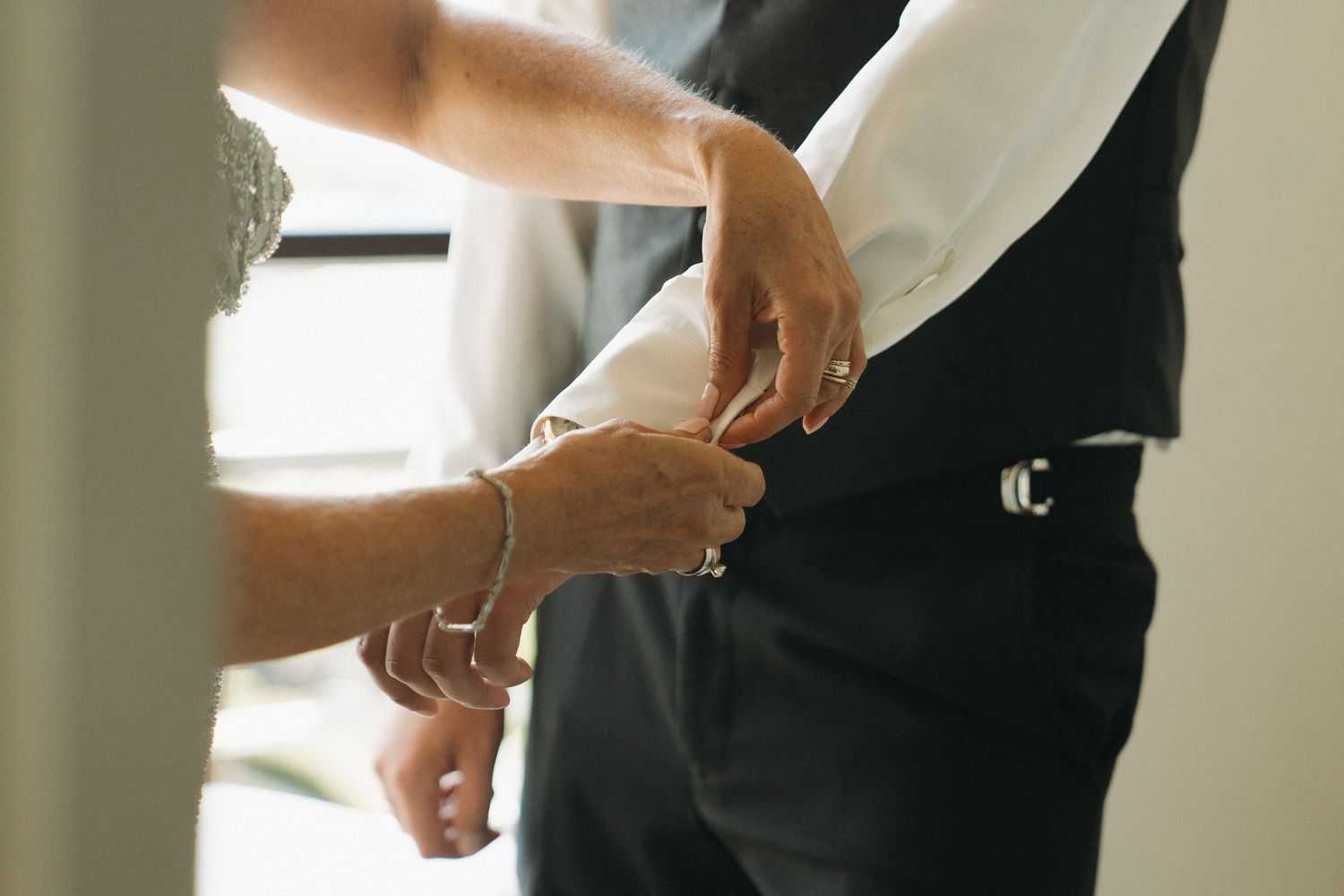 A person fastening cufflinks on a groom's white dress shirt sleeve before a wedding ceremony.