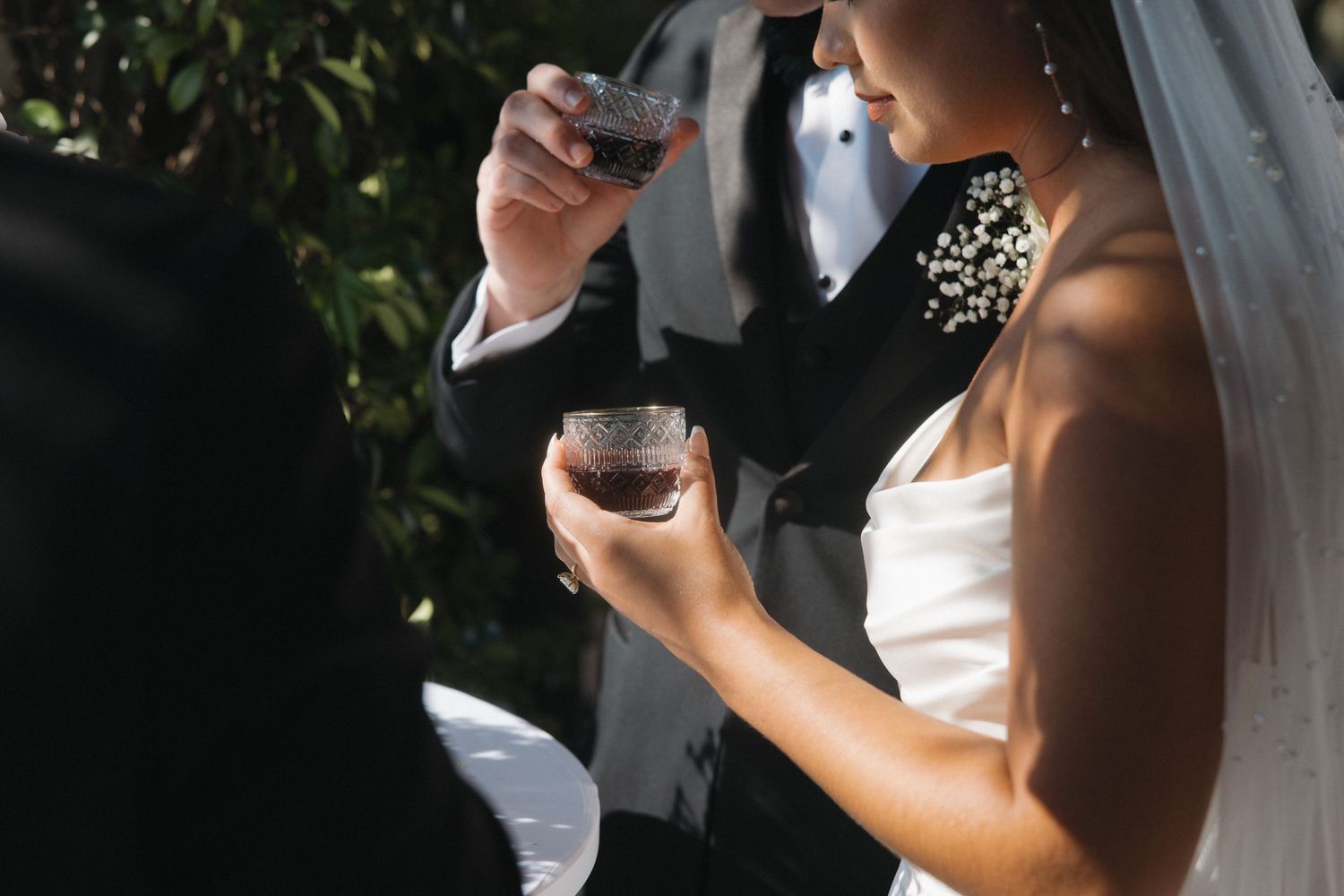Bride and groom holding glasses of red wine during outdoor wedding ceremony.