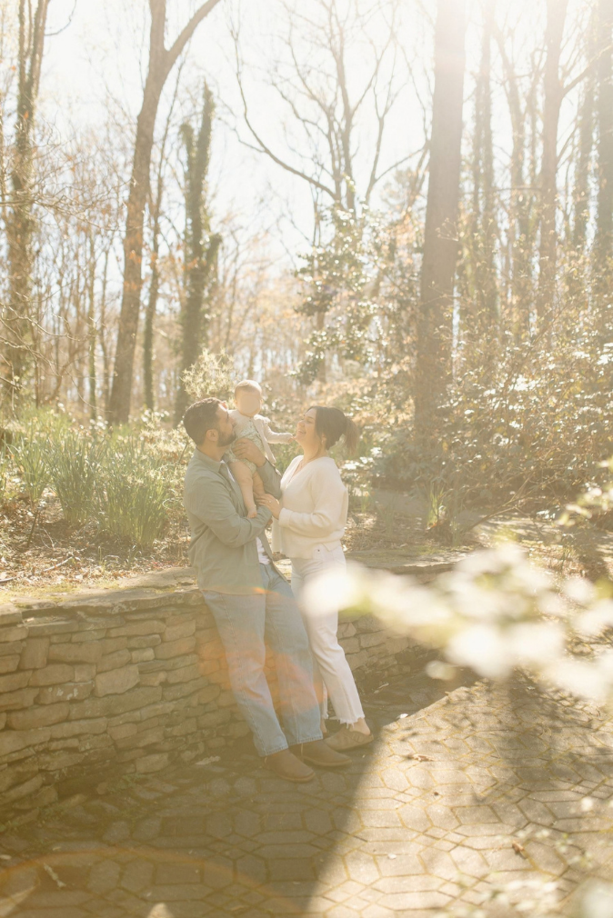 A family with a baby enjoys a sunny forest path, bathed in warm golden light among autumn trees.