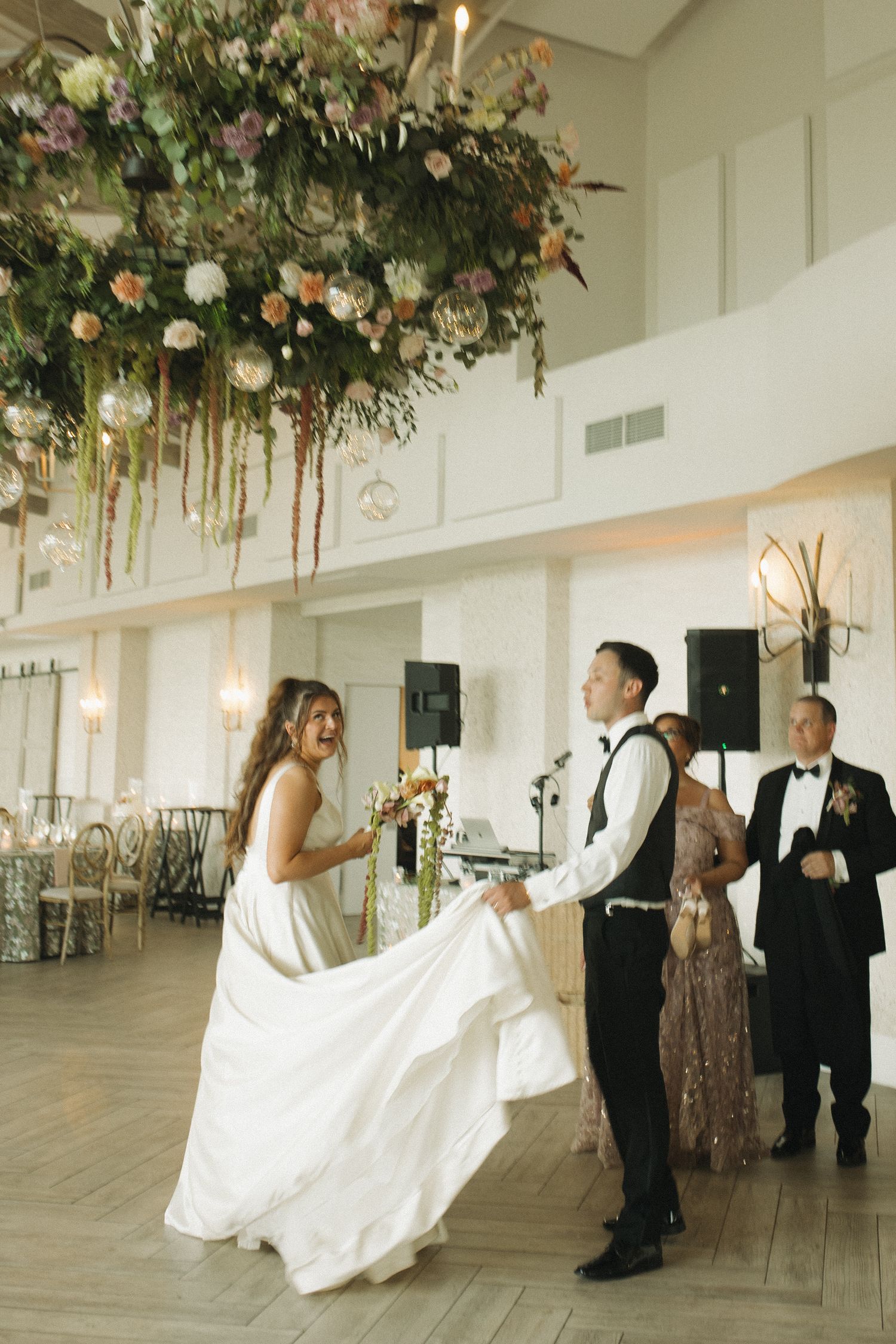 Bride and groom share their first dance under a lush floral chandelier in an elegant wedding reception venue.