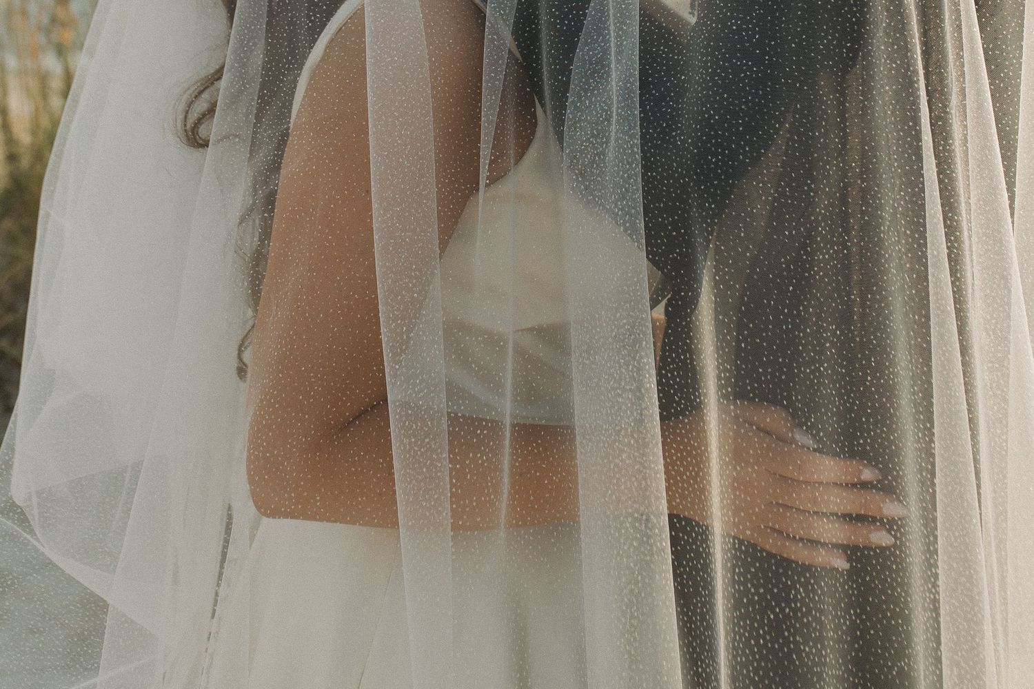 A bride and groom stand close together beneath a flowing sheer wedding veil, capturing an intimate romantic moment.