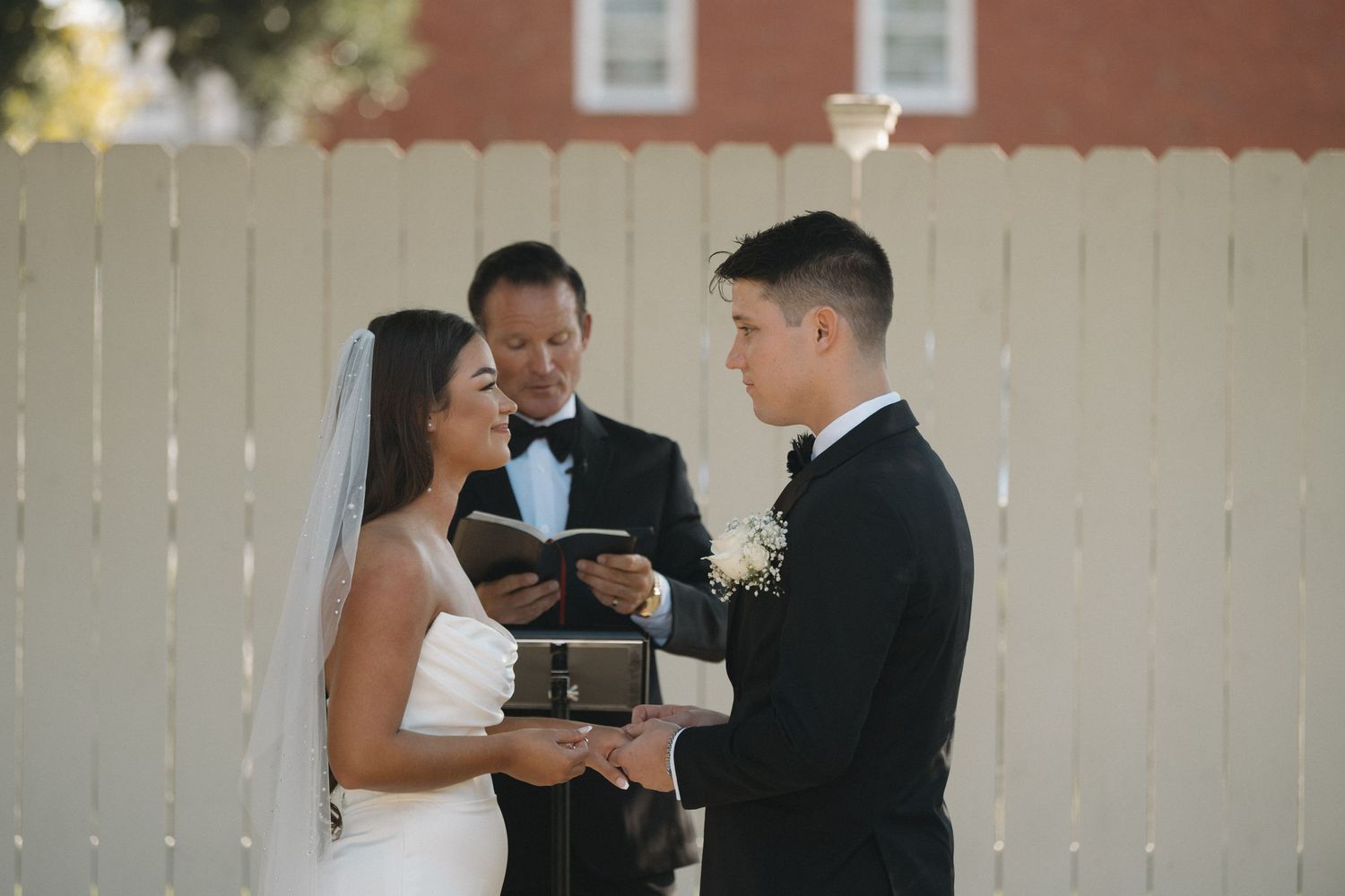 Bride and groom exchange vows outdoors at a wedding ceremony with an officiant holding a book.