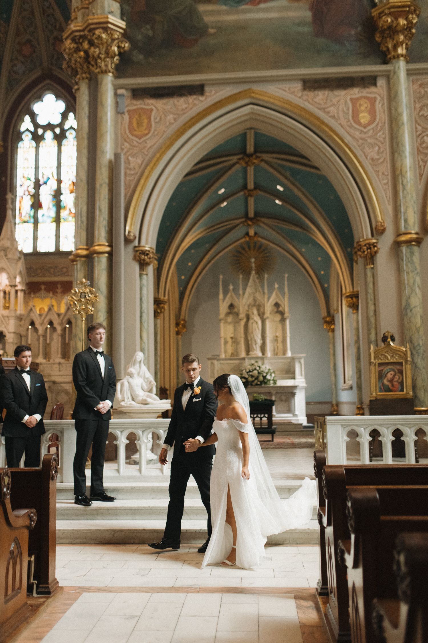 A bride and groom walk down the aisle of an ornate Gothic church during their wedding ceremony.