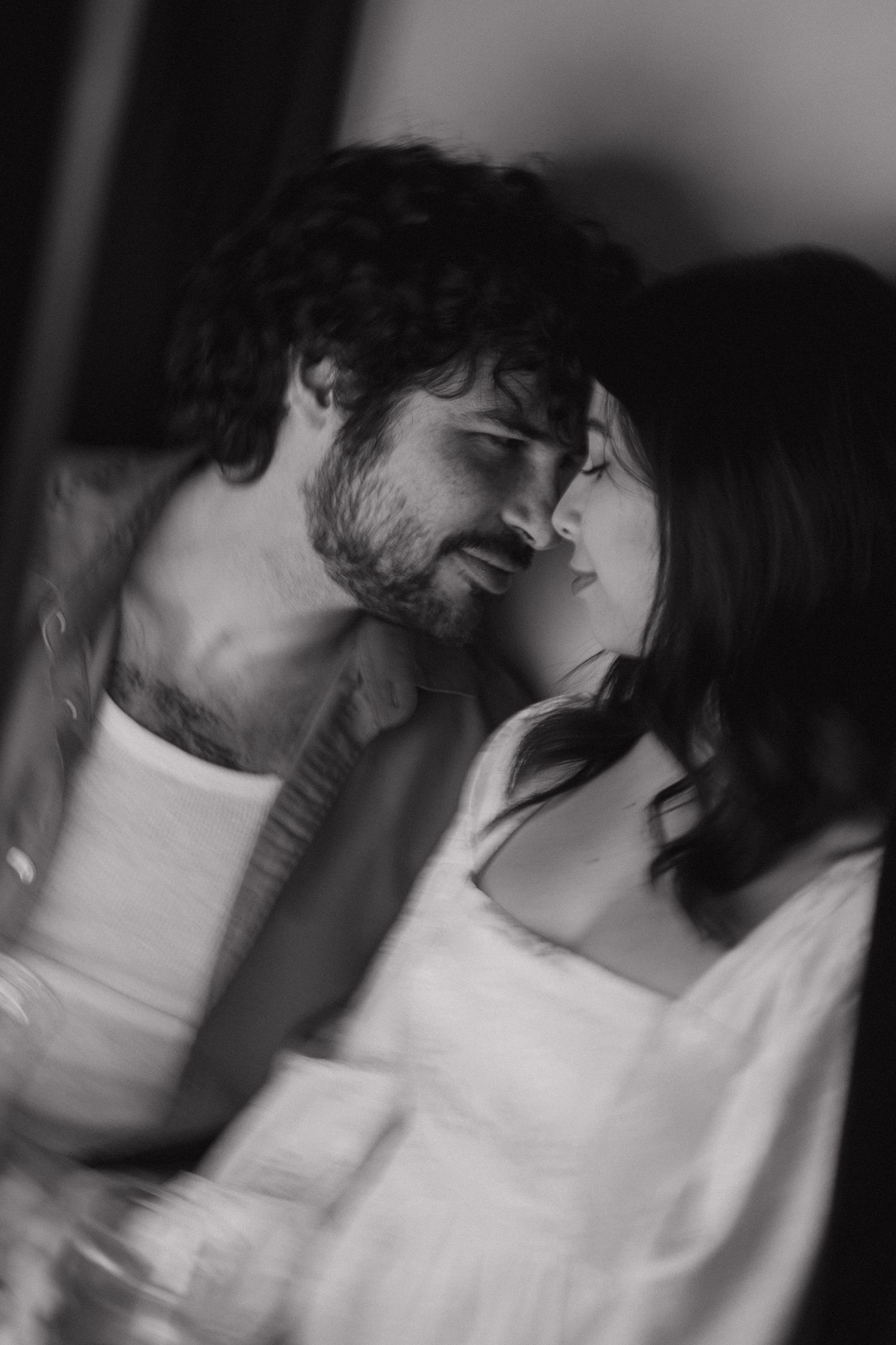 Black and white portrait of a couple gazing at each other in soft light.