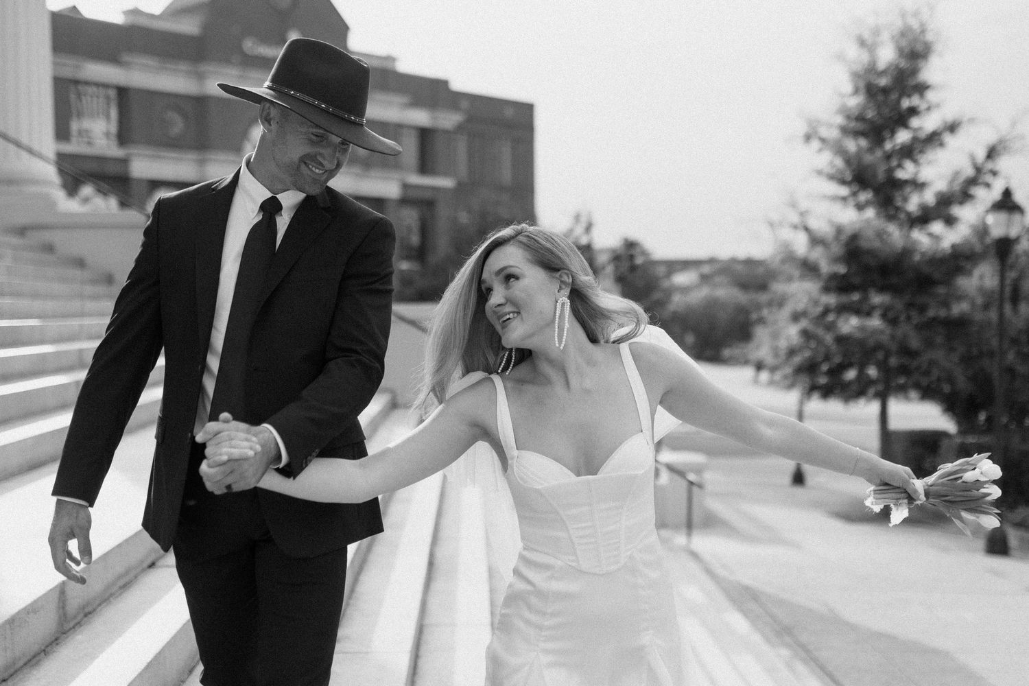 Black and white photo of smiling bride and groom walking down outdoor steps hand in hand.