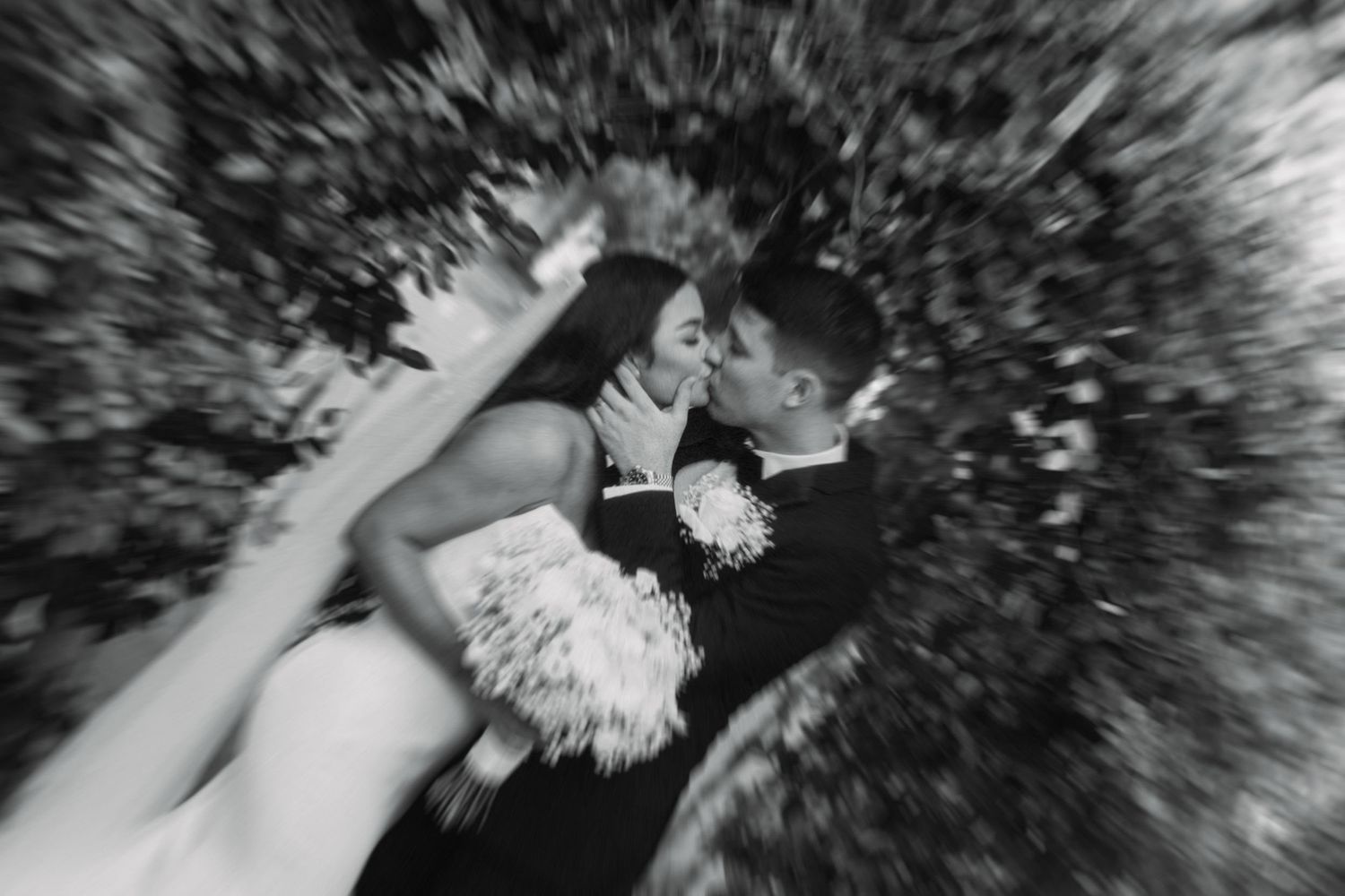 Bride and groom share passionate kiss in dramatic black and white wedding portrait outdoors.