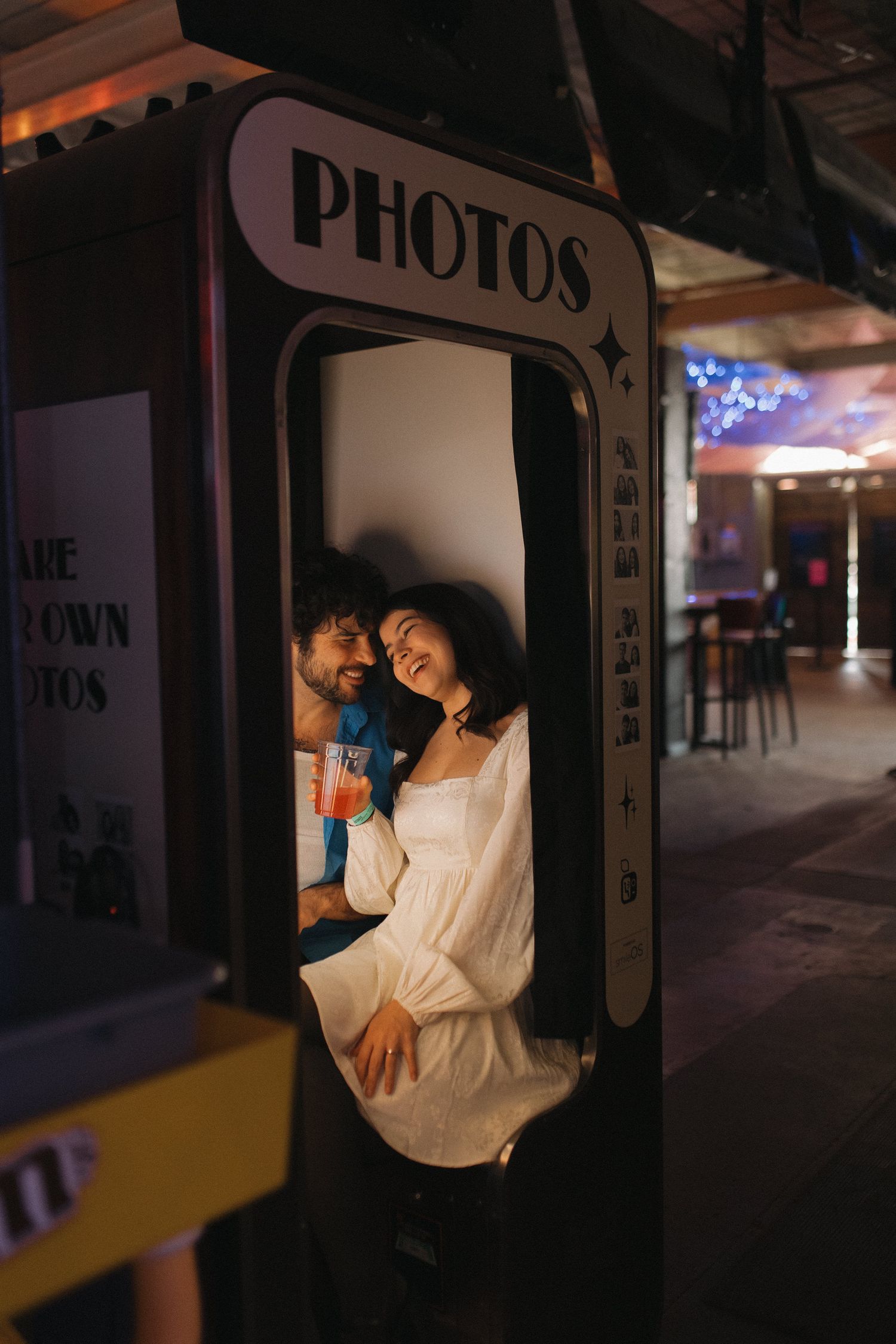 Smiling couple poses together inside a vintage photo booth at a venue.