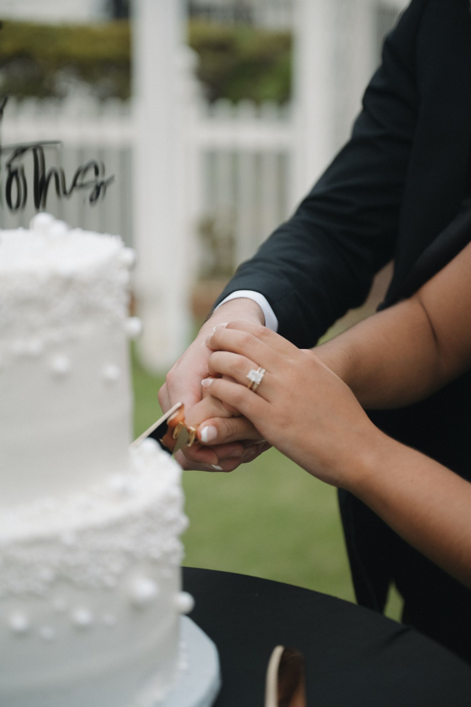 Close-up of bride and groom cutting white tiered wedding cake together with gold knife.