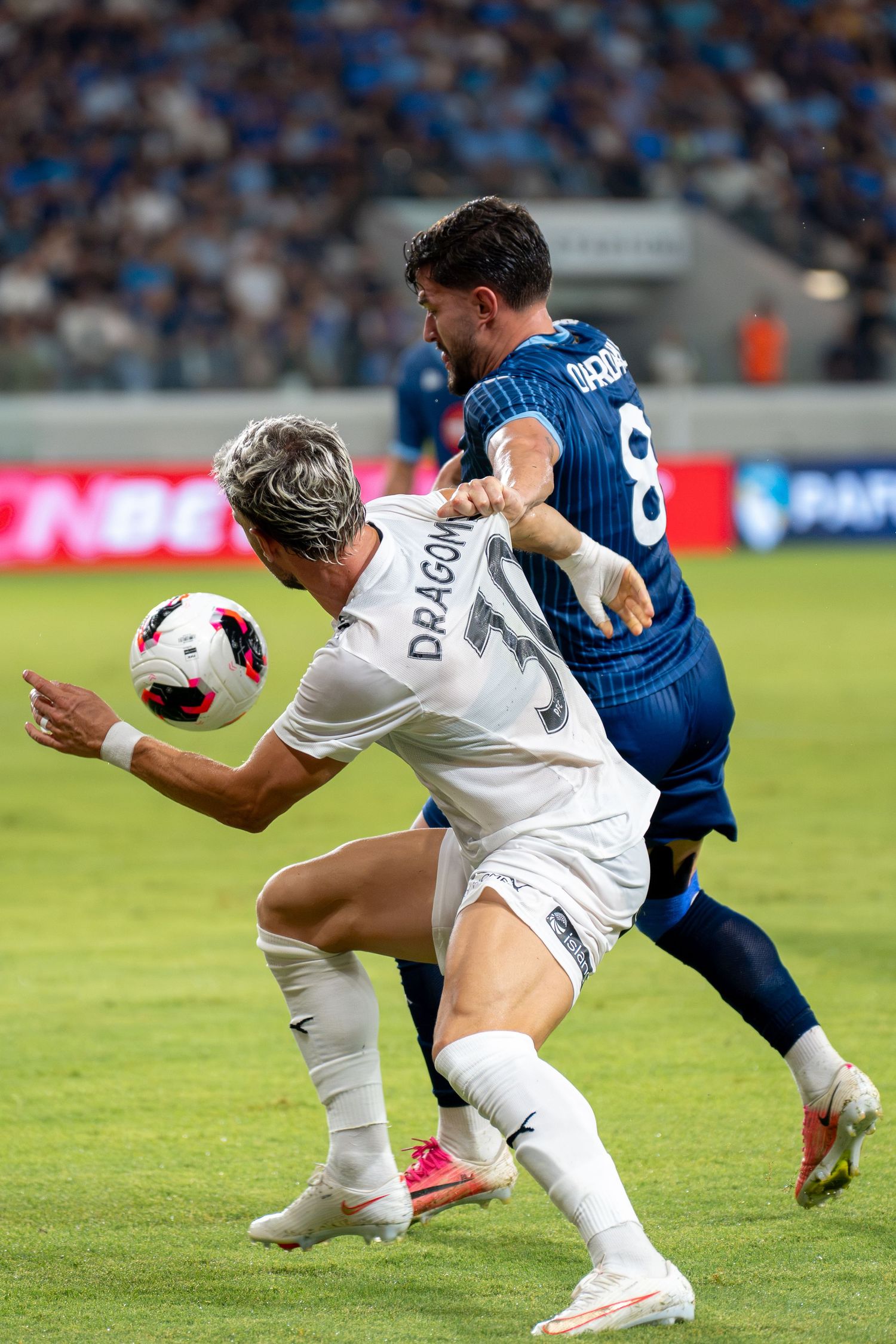 Two soccer players compete for the ball during an intense match in a packed stadium.