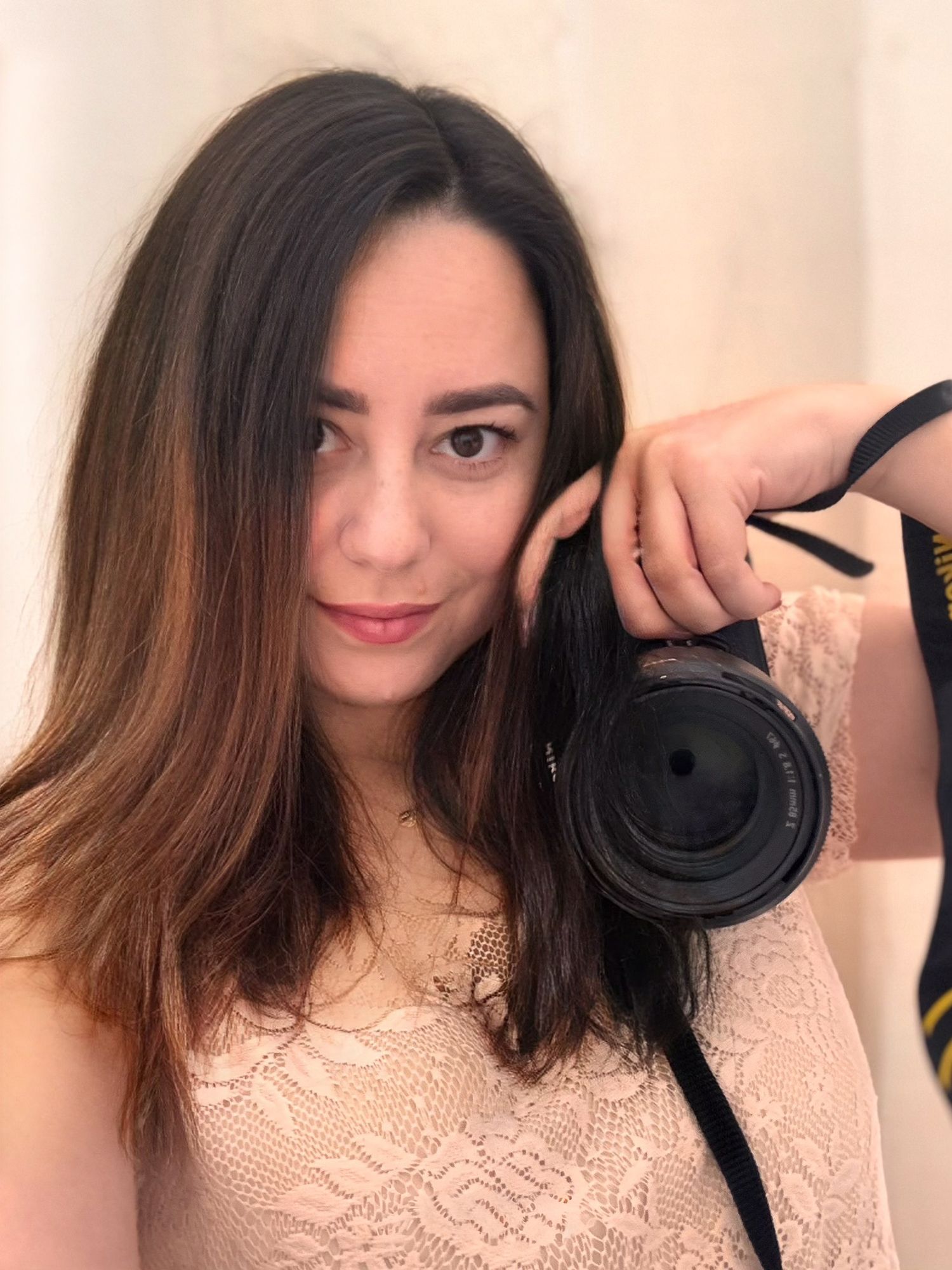 Young woman photographer holding DSLR camera taking a selfie in mirror indoors.