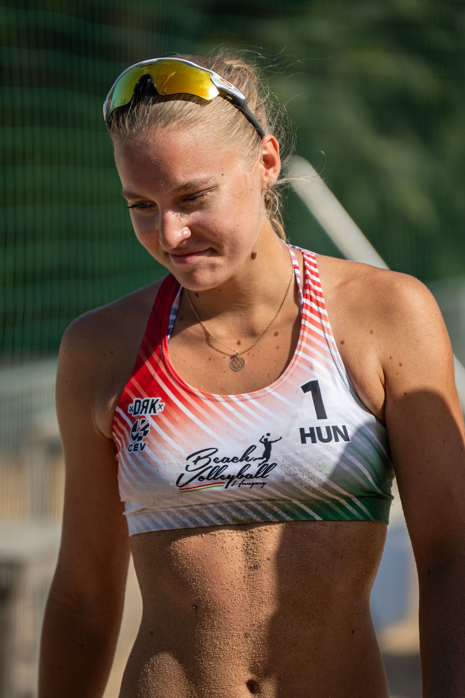 Female beach volleyball player wearing HUN jersey and sunglasses on sandy court during competition.