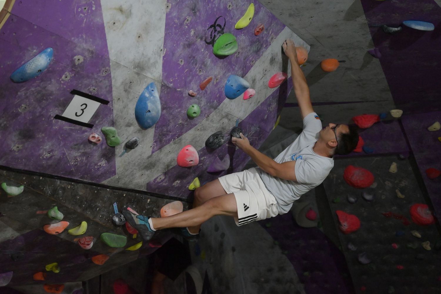 Male climber scaling colorful overhang route on indoor bouldering wall at gym.