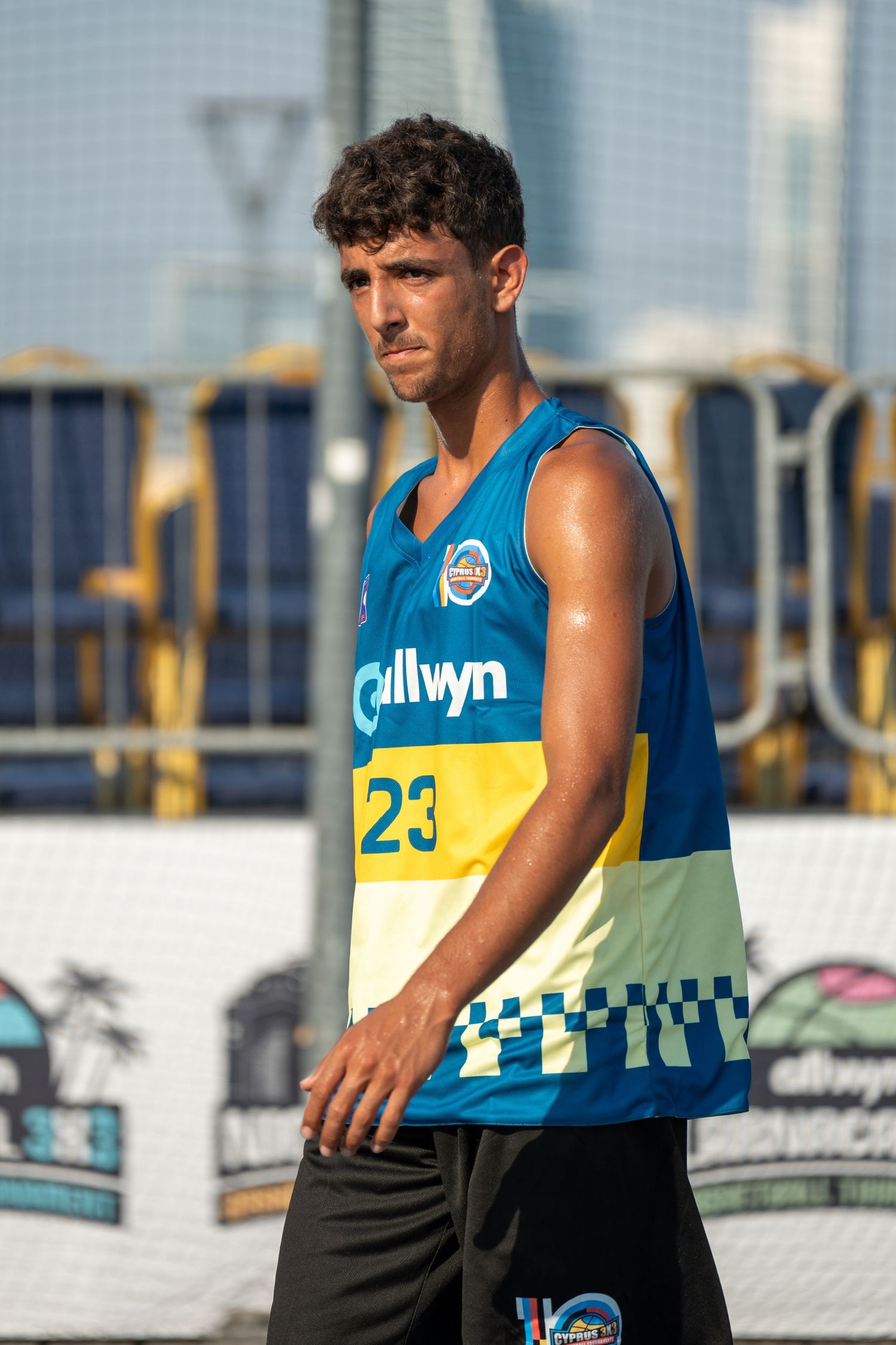 Male basketball player number 23 in Allwyn blue and yellow jersey on outdoor 3x3 court.