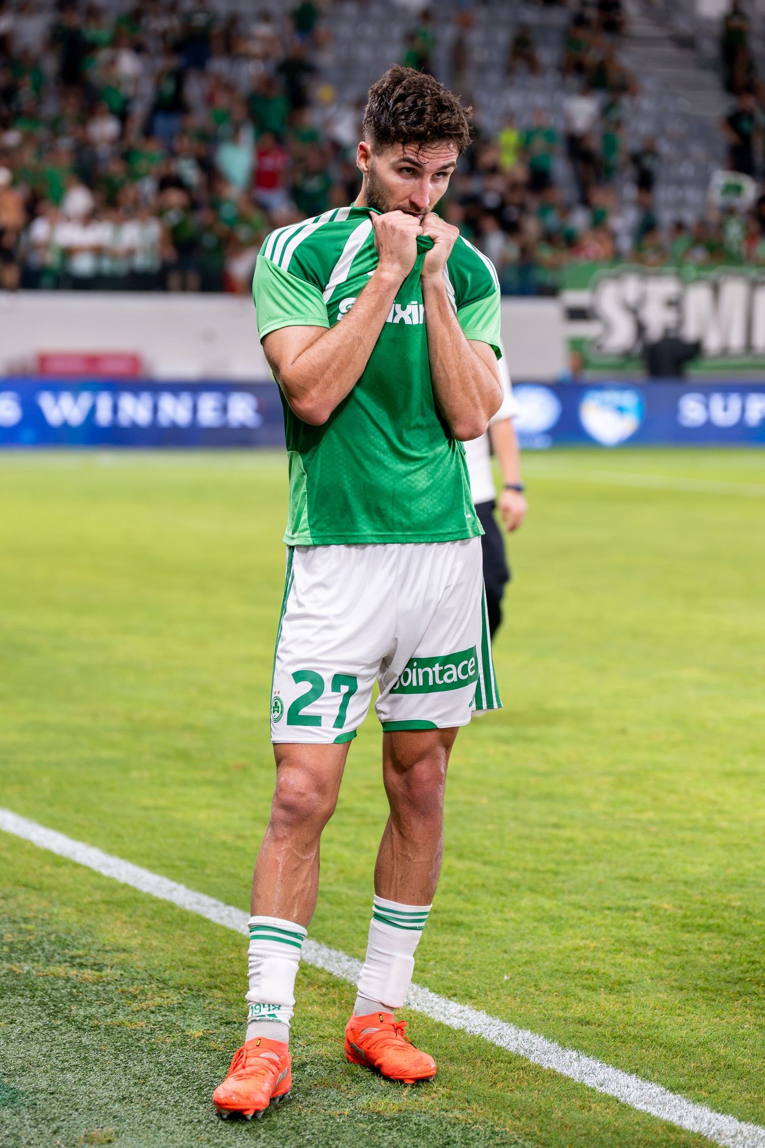 Football player in green and white kit number 27 celebrating on the pitch during a match.