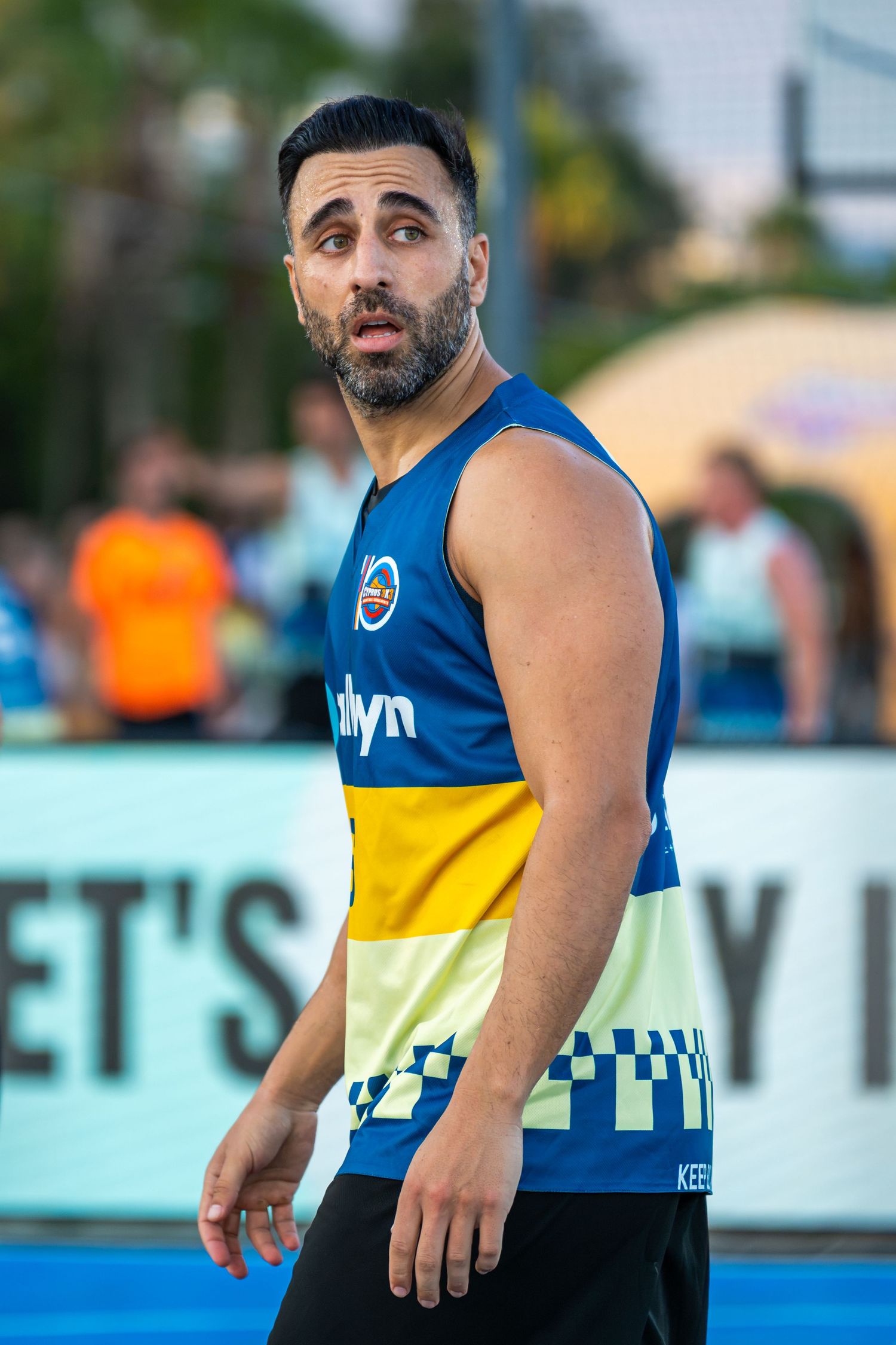 Male basketball player in blue and yellow Brooklyn jersey with surprised expression on outdoor court.