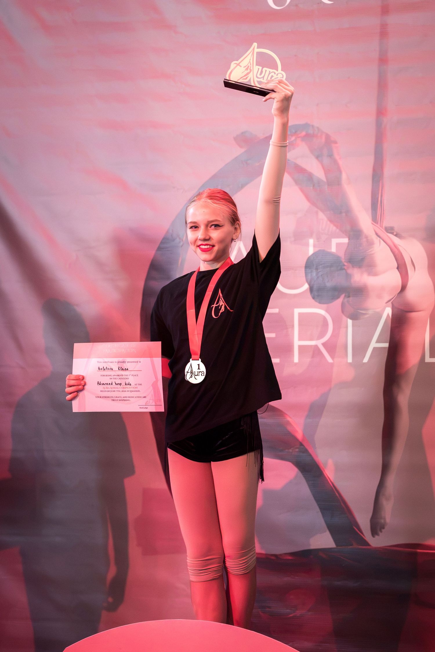 Young female aerial arts competitor proudly holding a trophy and certificate at an Aura Aerial event.