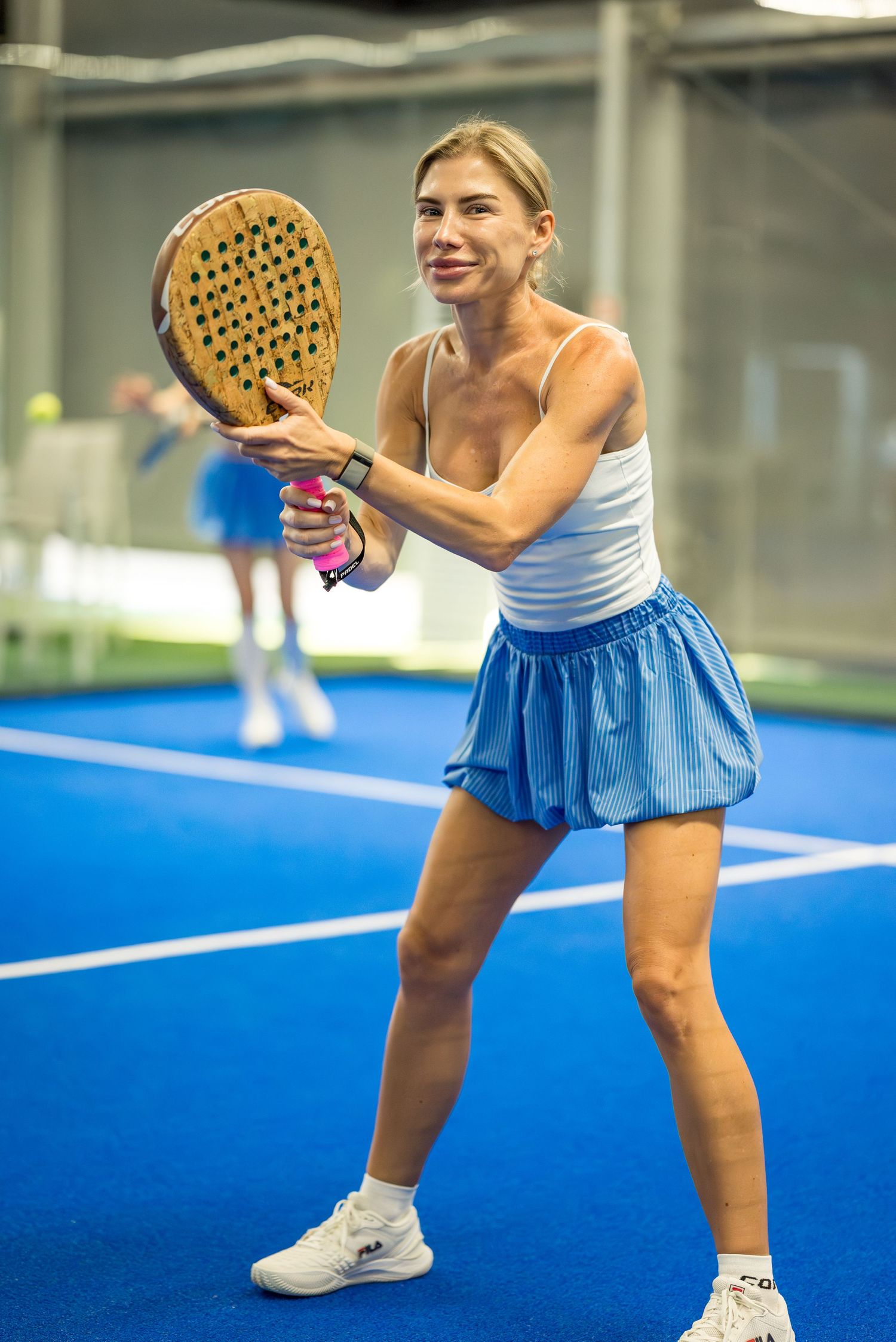 Athletic woman playing padel tennis in blue skirt swinging racket on indoor blue court.