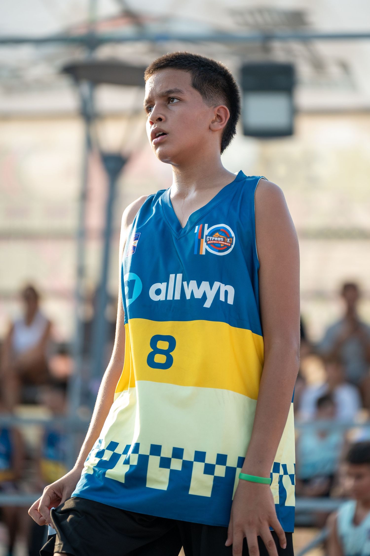 Young male basketball player number 8 in Allwyn blue and yellow jersey on outdoor court.