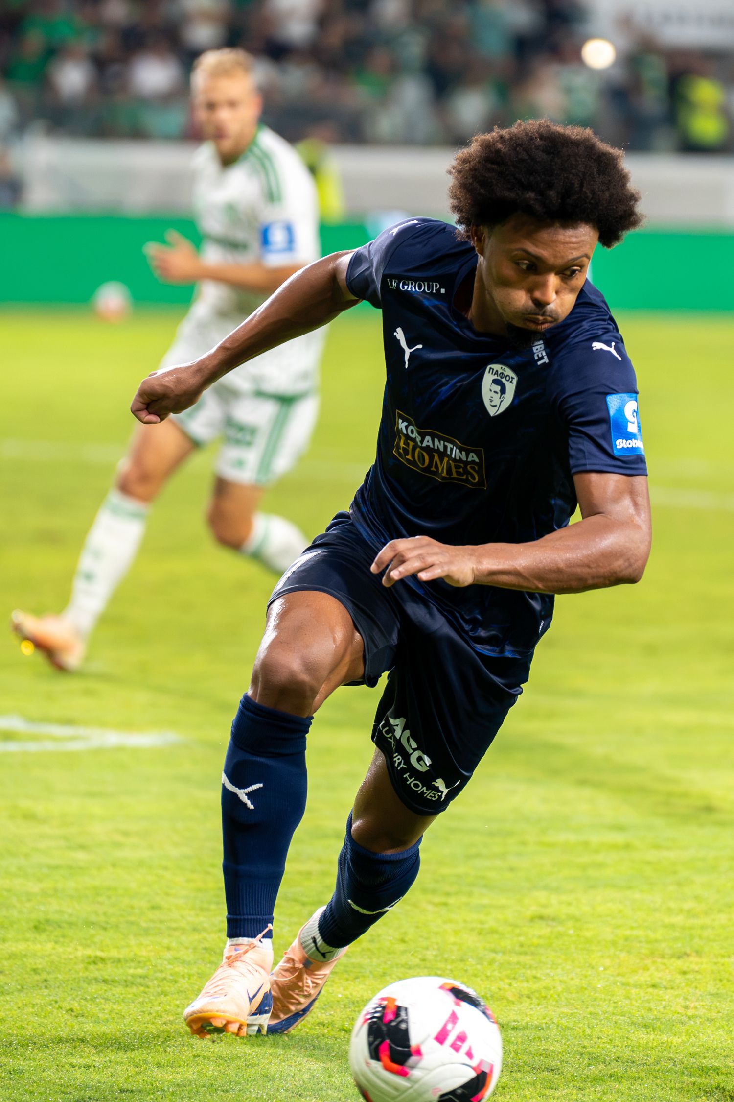 A soccer player in a navy blue Puma kit dribbles the ball during a professional football match.