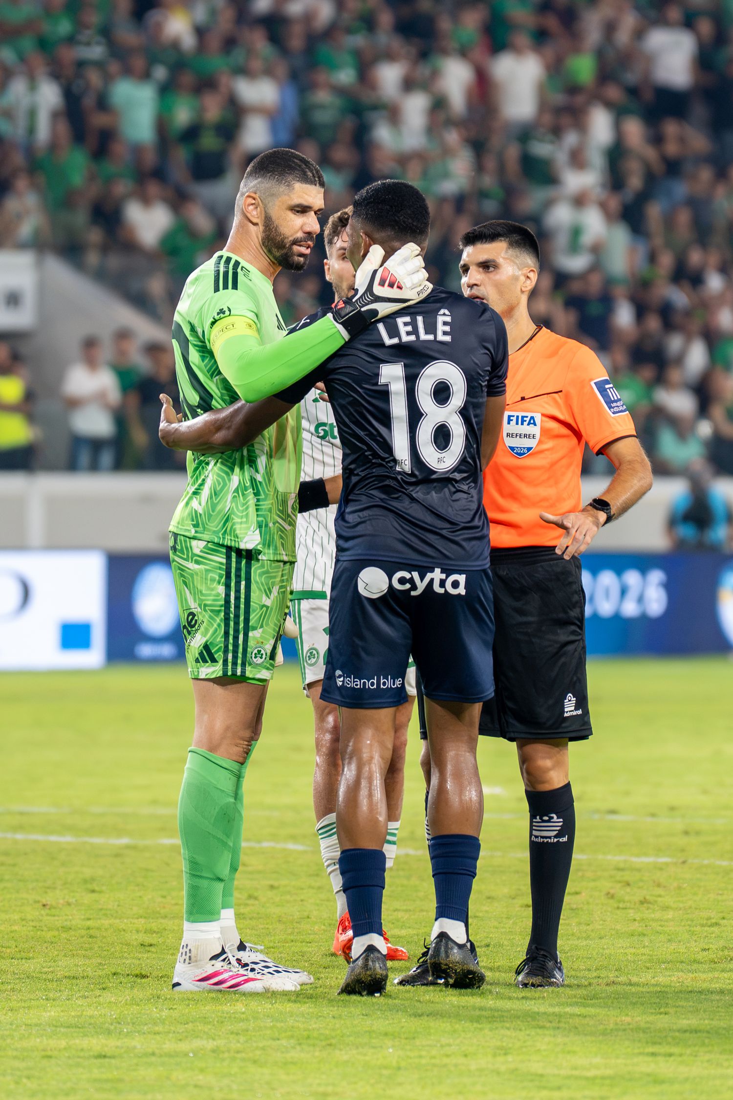 Two soccer players and FIFA referee interact on field during a competitive football match.