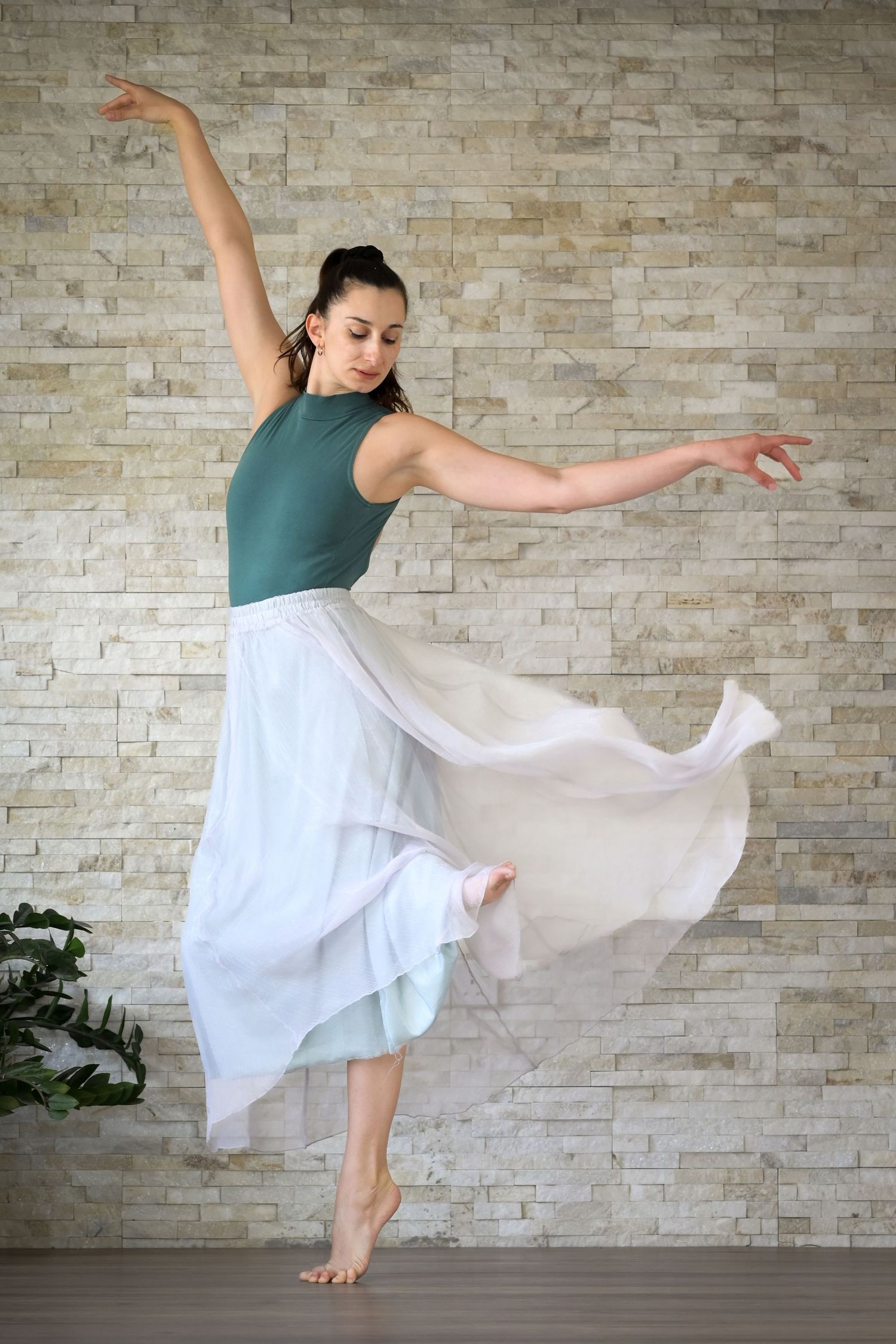 Female dancer performing graceful contemporary dance in flowing white skirt in studio.