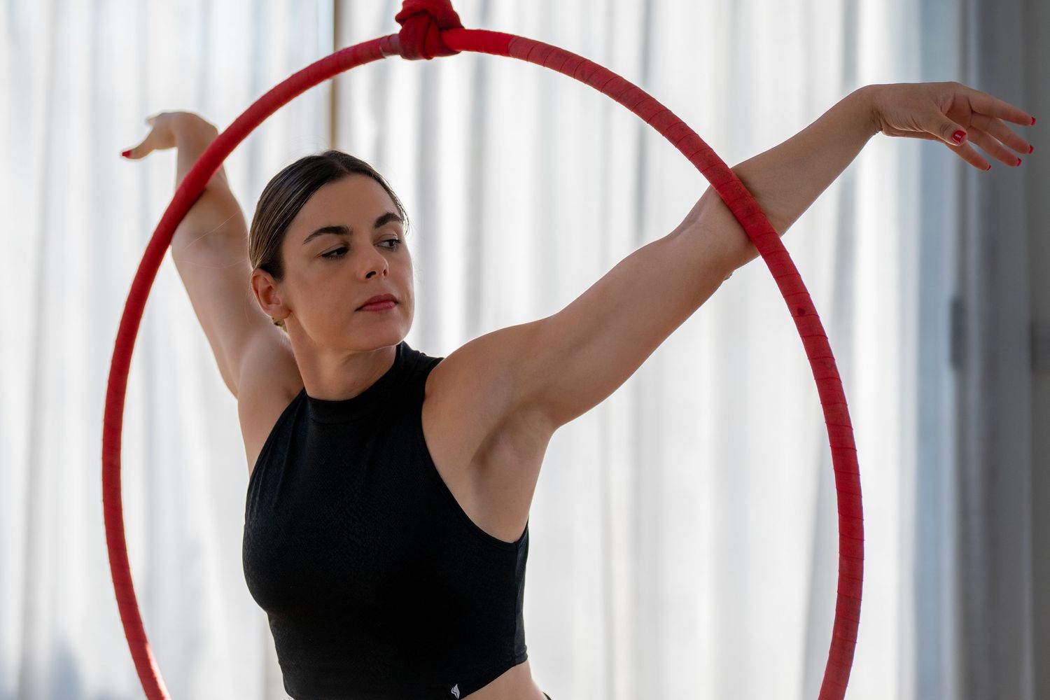 Female aerial hoop lyra circus artist balancing gracefully inside red ring with arms extended.