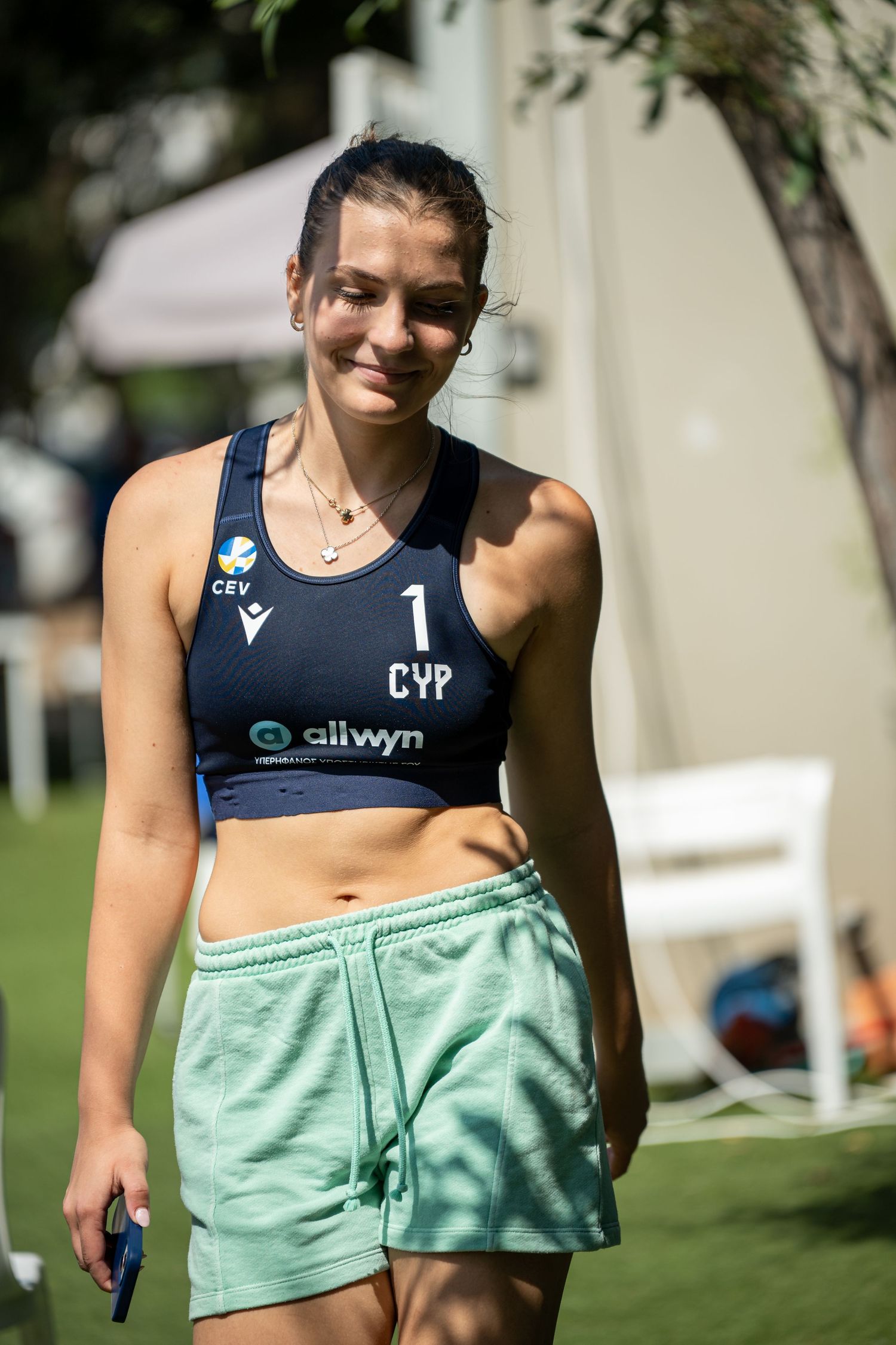Female beach volleyball player in CEV CYP navy top and mint shorts smiling outdoors at tournament.