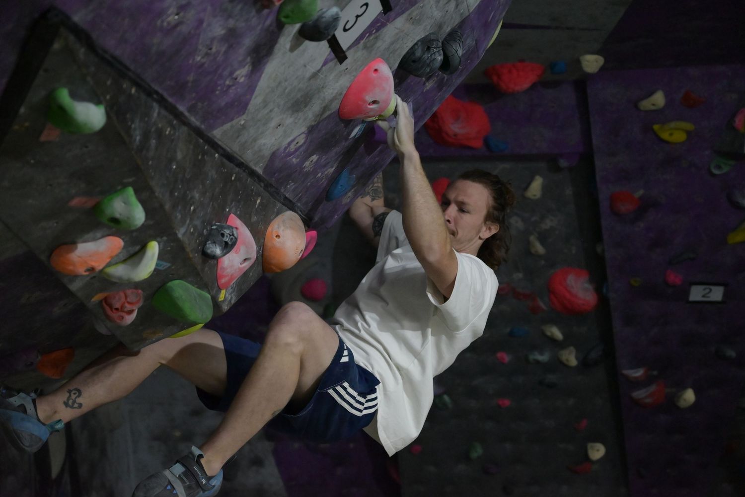 Young woman bouldering on colorful indoor climbing wall at climbing gym.