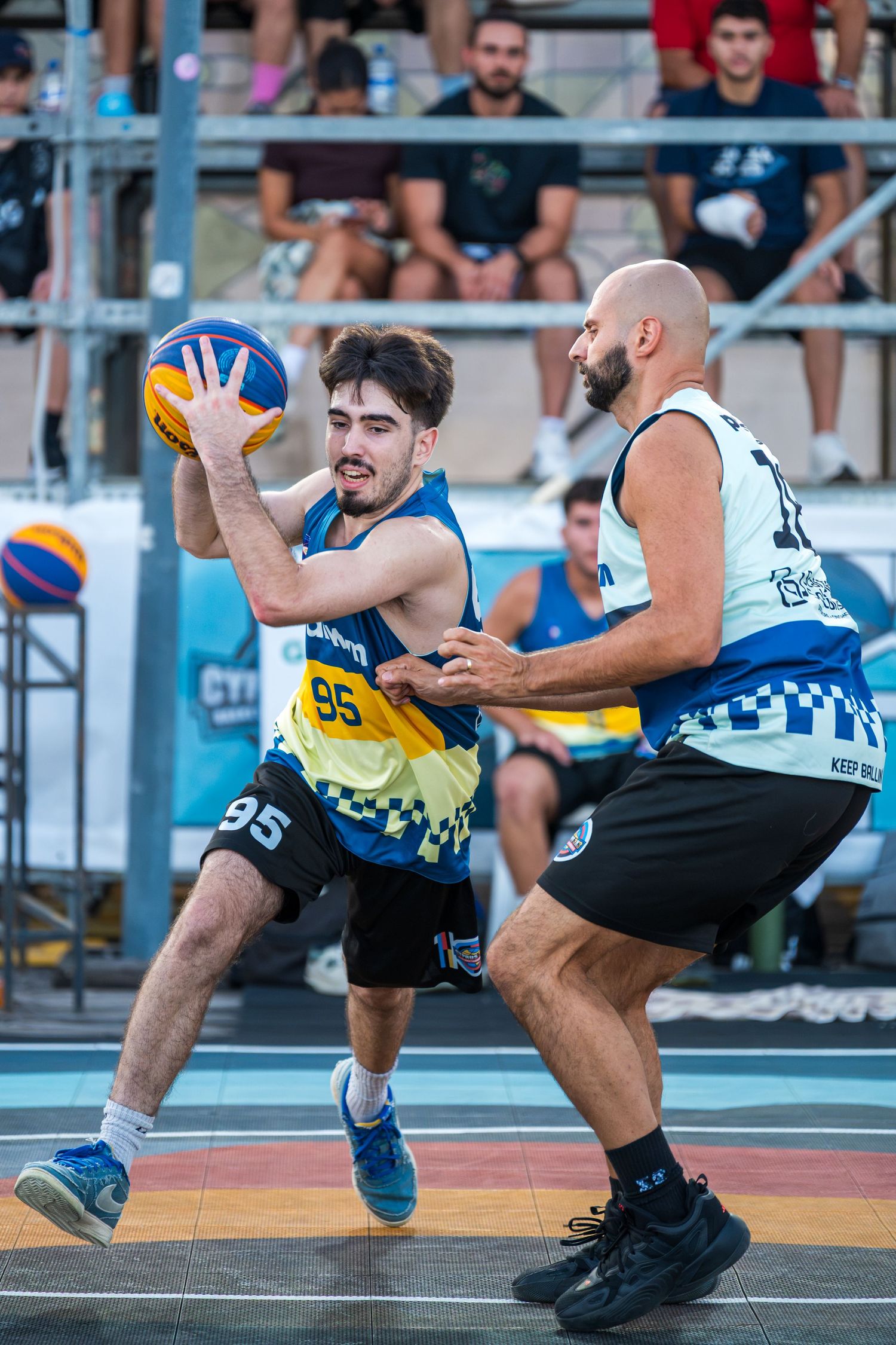 A basketball player wearing number 95 looks to pass while being defended in a 3x3 outdoor tournament.