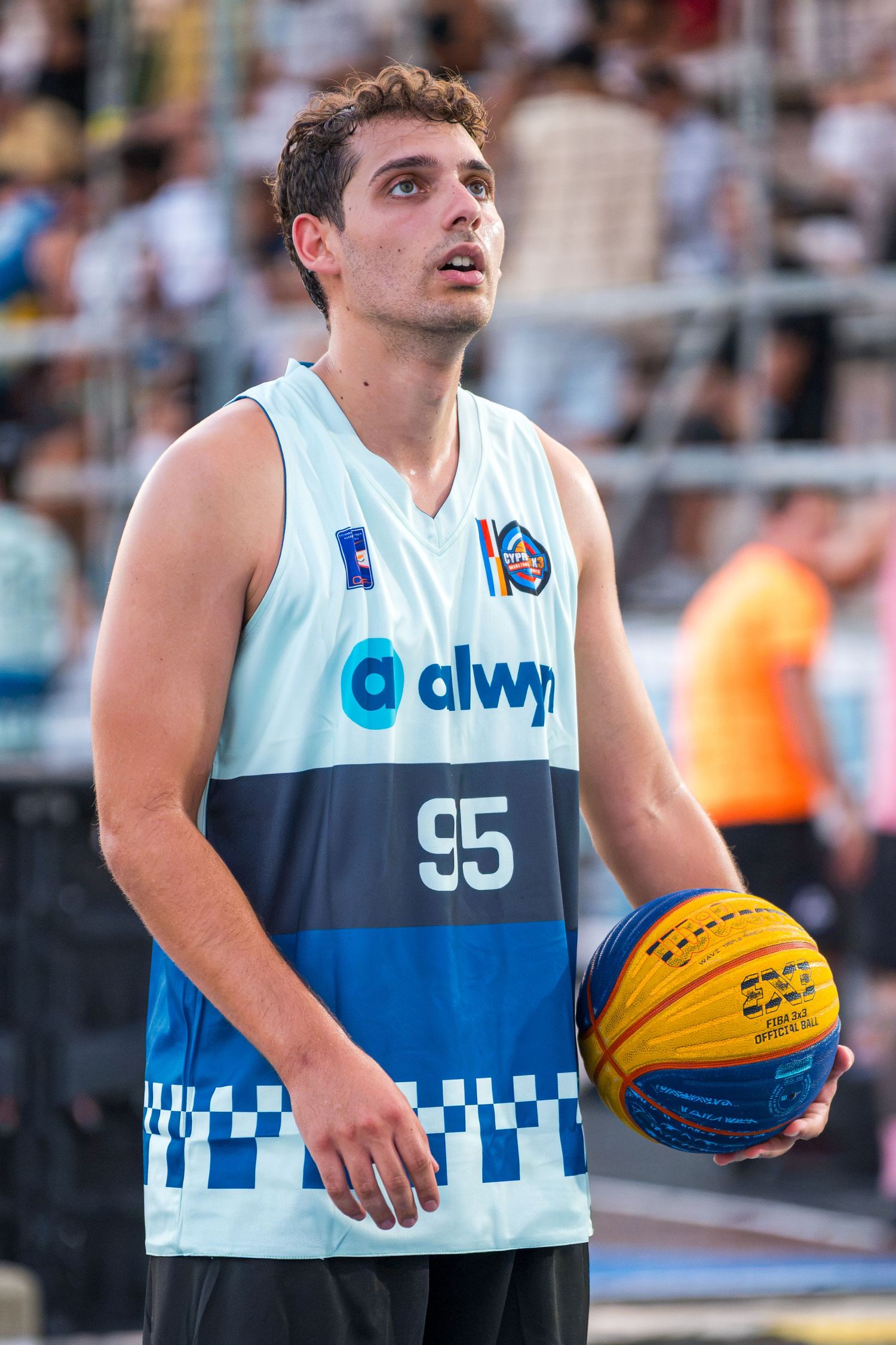 Young male basketball player number 95 in Alwyn jersey holding ball on outdoor 3x3 court.