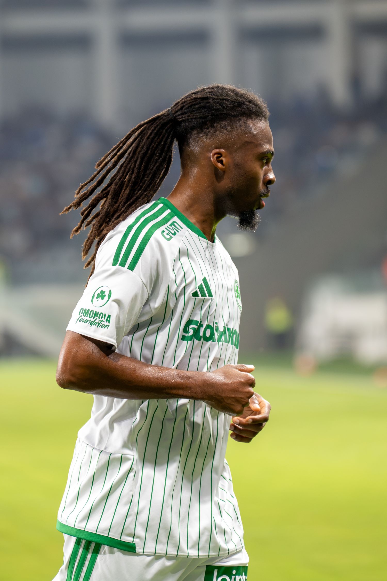 Soccer player with dreadlocks in white and green Panathinaikos jersey running during match.