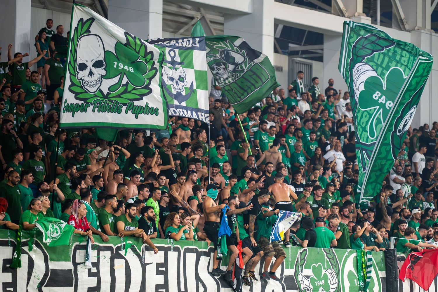 Green-clad soccer fans waving flags and banners in a stadium stand during a match.