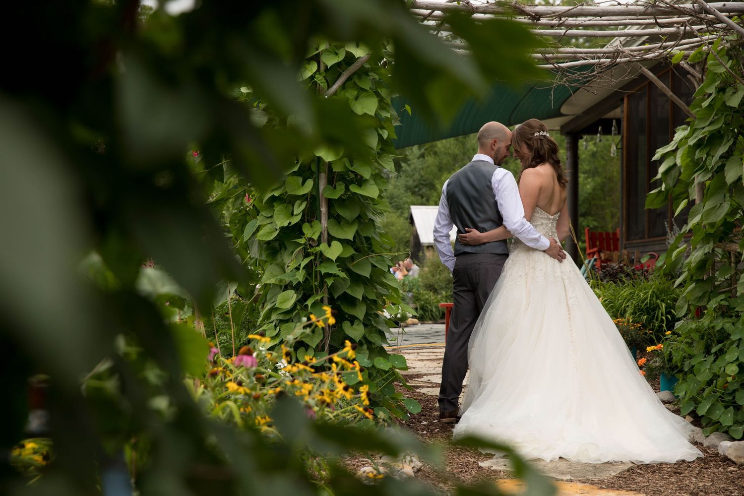 Bride and groom sharing intimate moment in lush garden framed by green foliage.