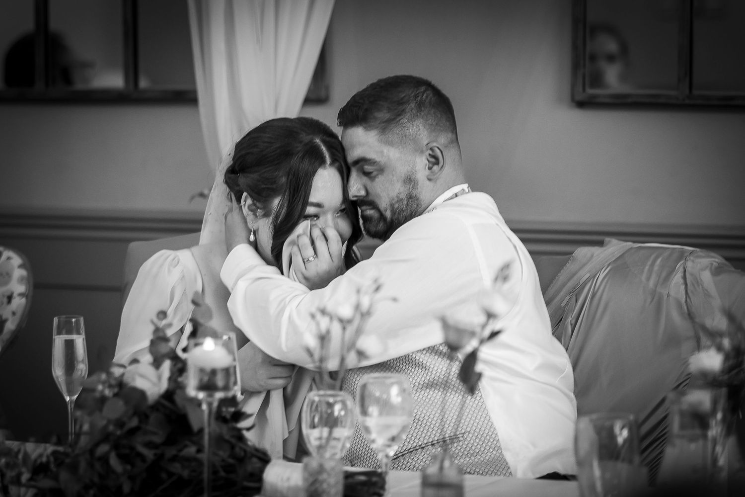 Black and White image of the groom consoling his bride during an emotional speech by her father