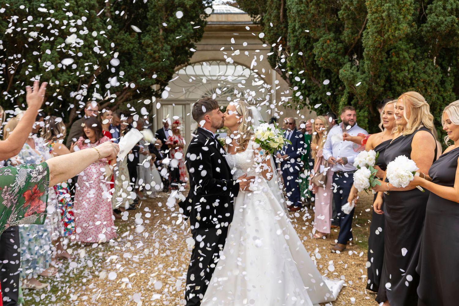 A just married bride and groom pause mid confetti nthrowing for a quick kiss