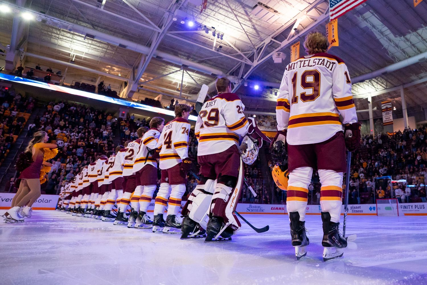 Minnesota Gophers hockey team lines up on ice during a packed arena game, players wearing maroon and gold jerseys.