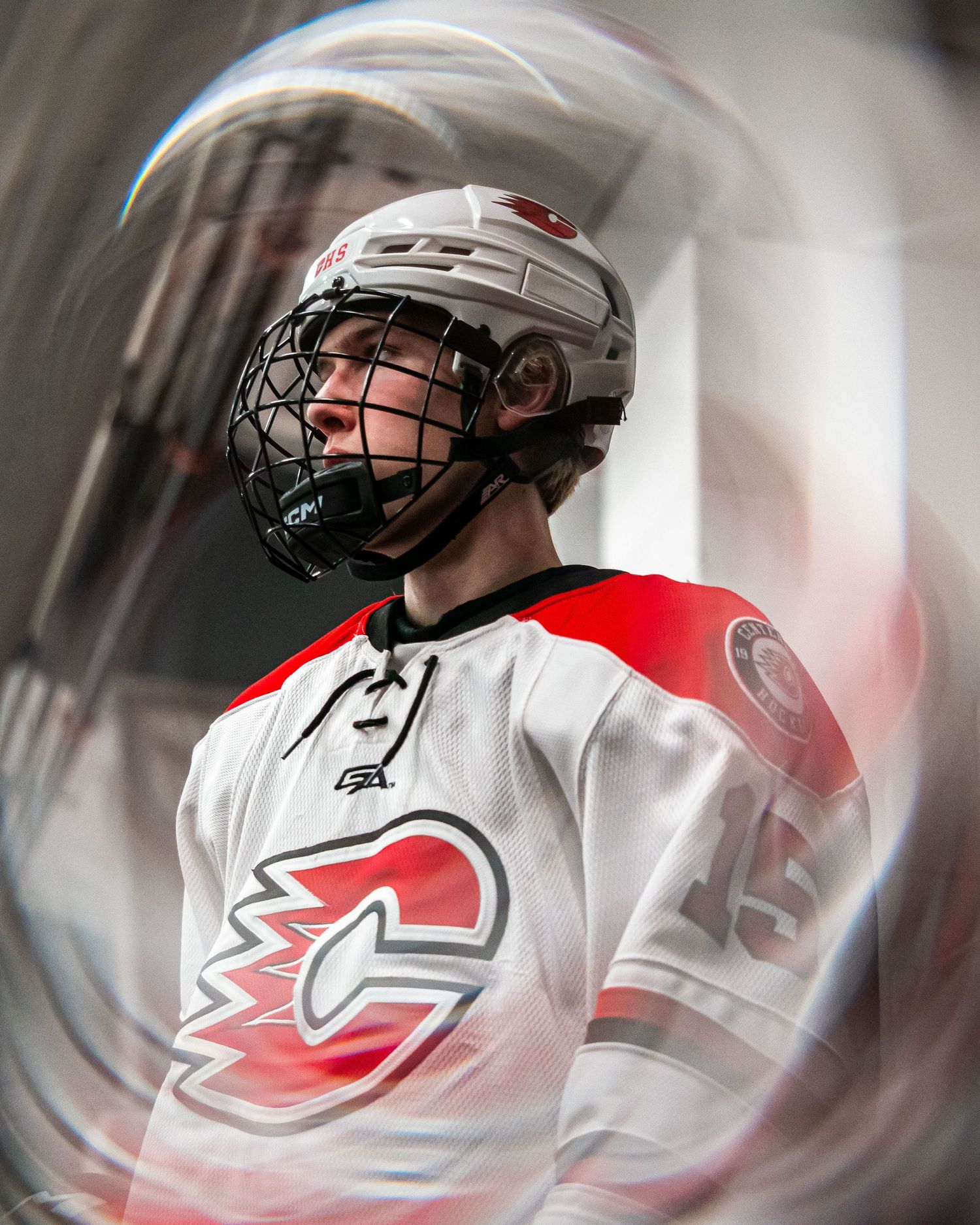 Young hockey player in white Calgary Flames jersey and helmet poses dramatically in arena tunnel with swirling lens effect.