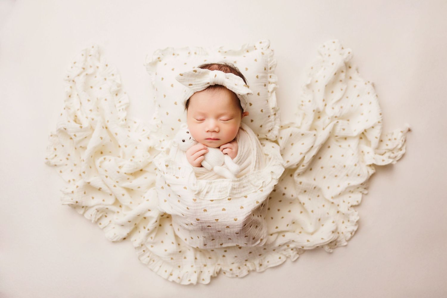 Newborn baby wrapped in white, resting among soft cream-colored fabric.