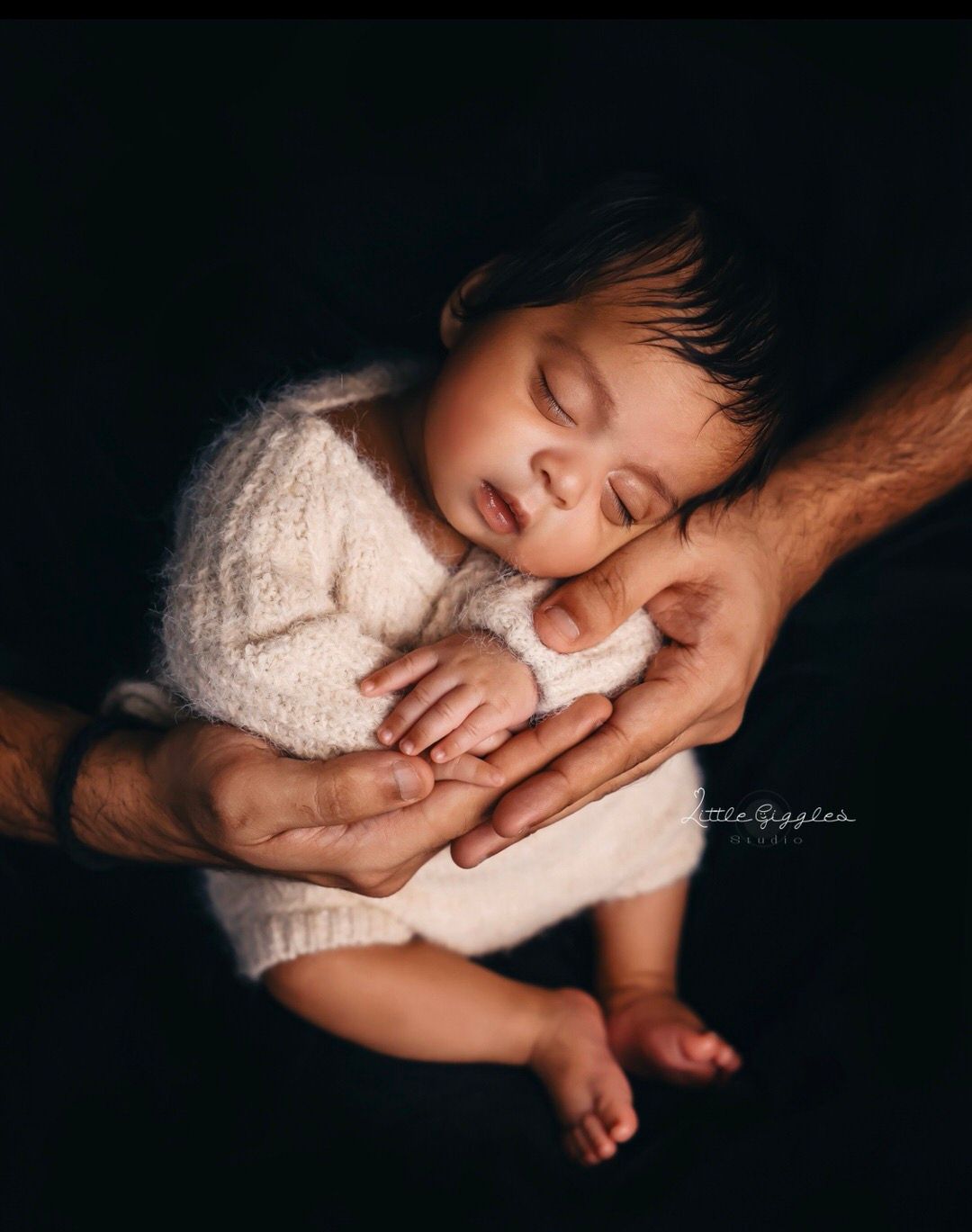 * Newborn curled peacefully in a parent’s arms against a dark background.
