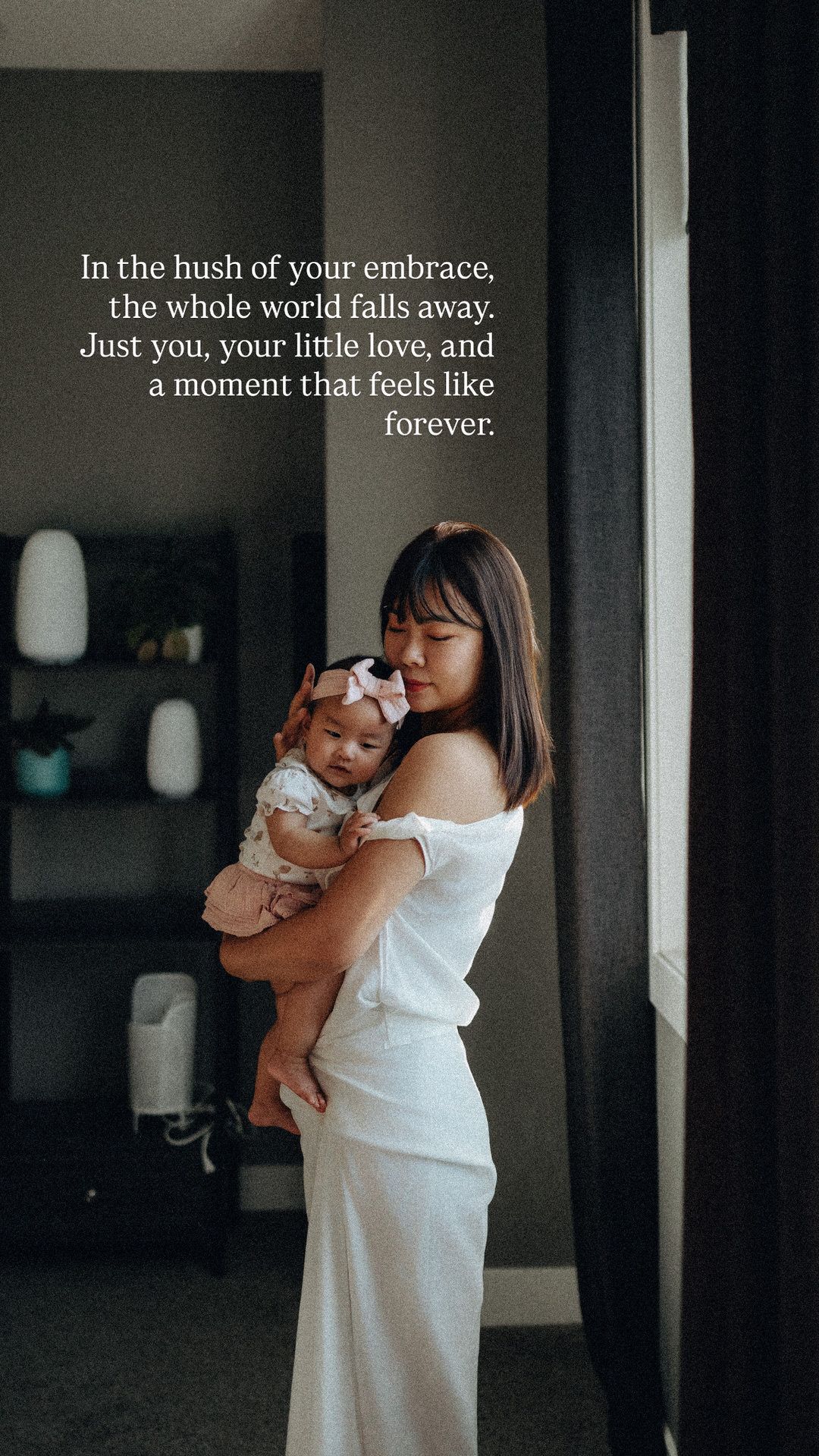 A mother in a white dress gently holds her baby girl in a softly lit room, with a heartfelt quote about a timeless embrace.